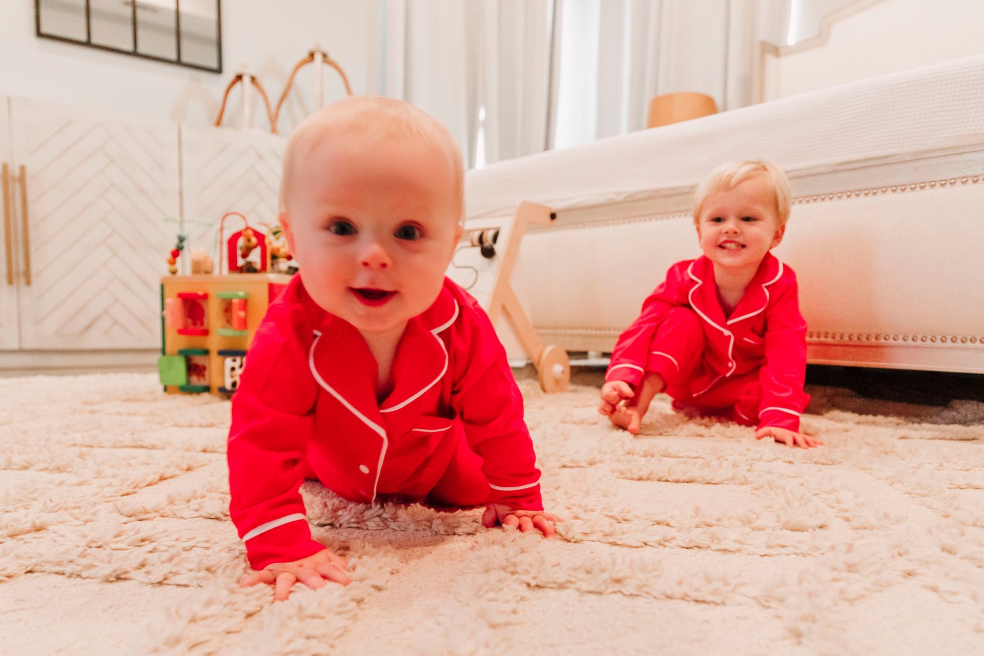 Two babies in red pajamas are crawling on the floor.
