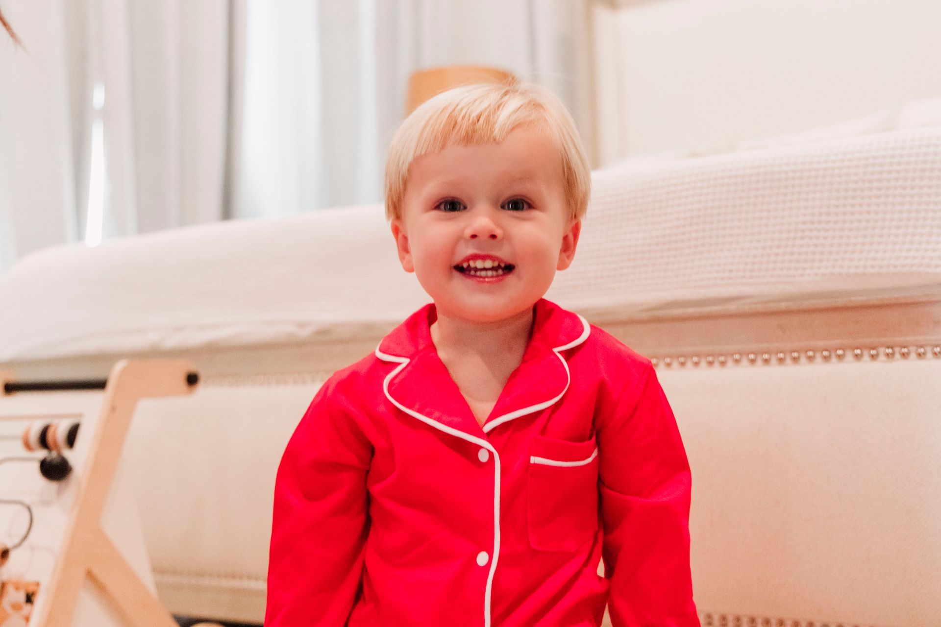 A little boy is wearing a red pajama set and smiling.
