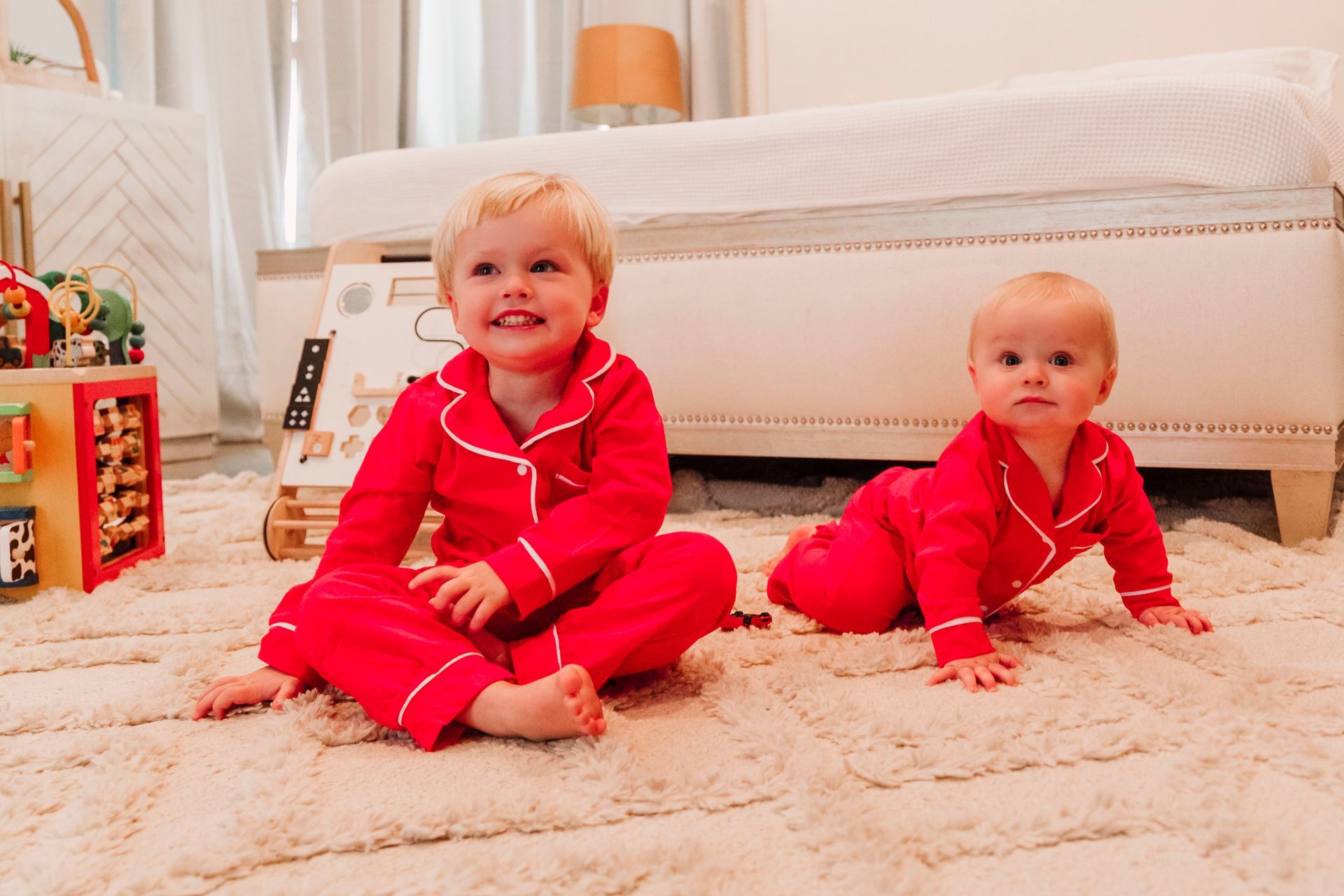 Two little boys are sitting on the floor wearing red pajamas.