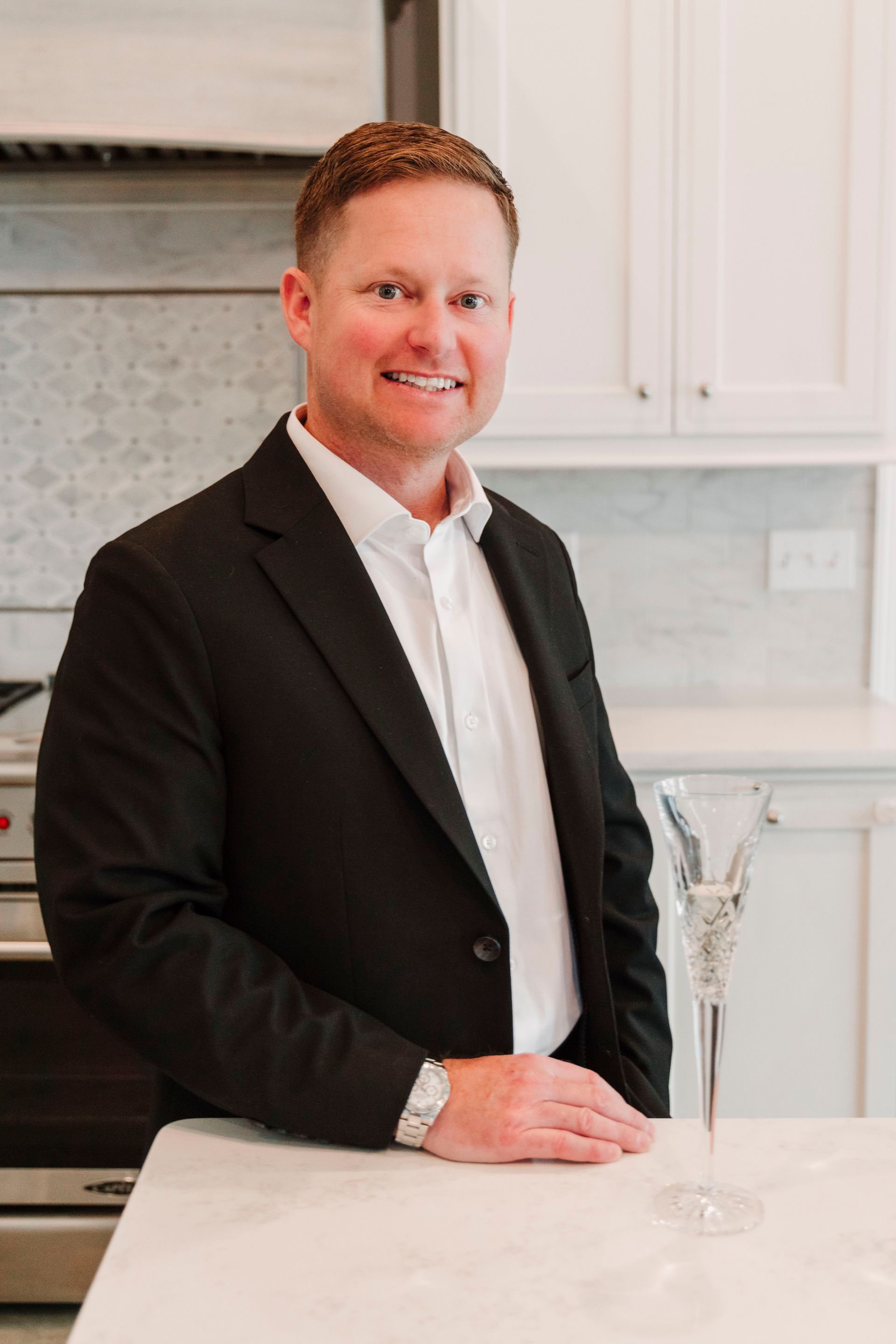 A man in a suit is standing next to a counter in a kitchen.