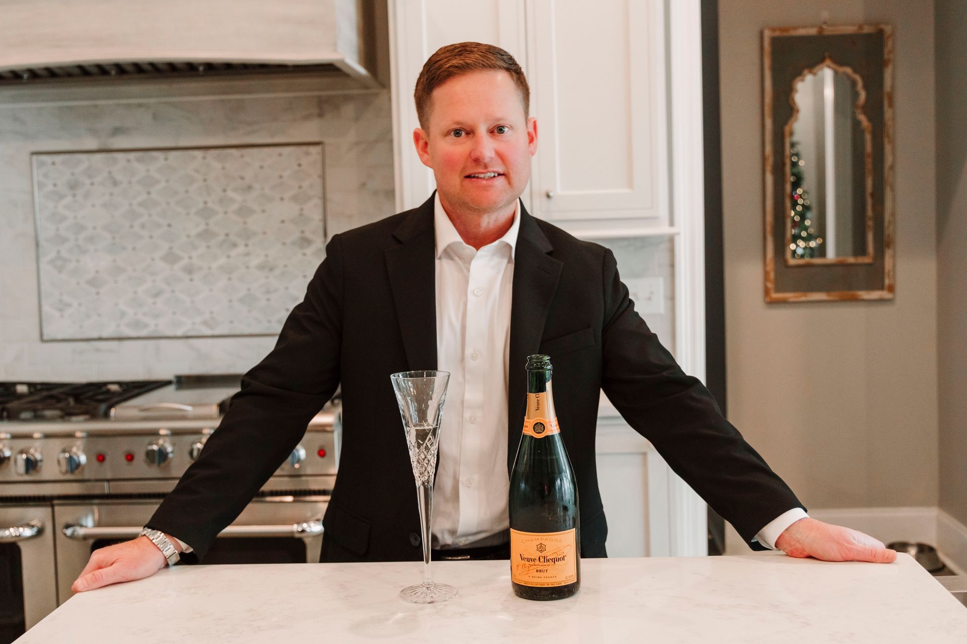 A man in a suit is standing next to a bottle of champagne and a glass.