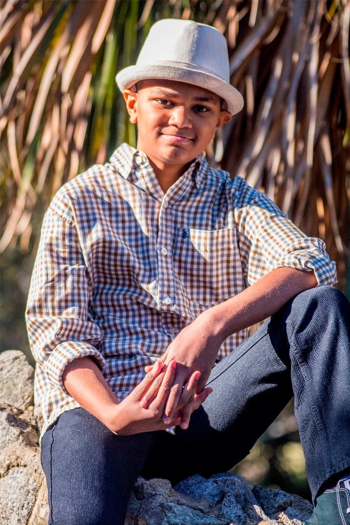 A young boy wearing a hat is sitting on a rock.