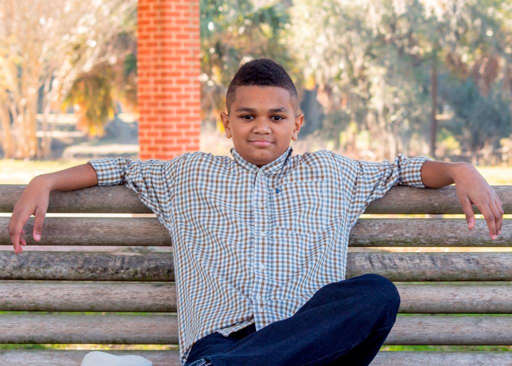 A young boy is sitting on a park bench with his legs crossed.