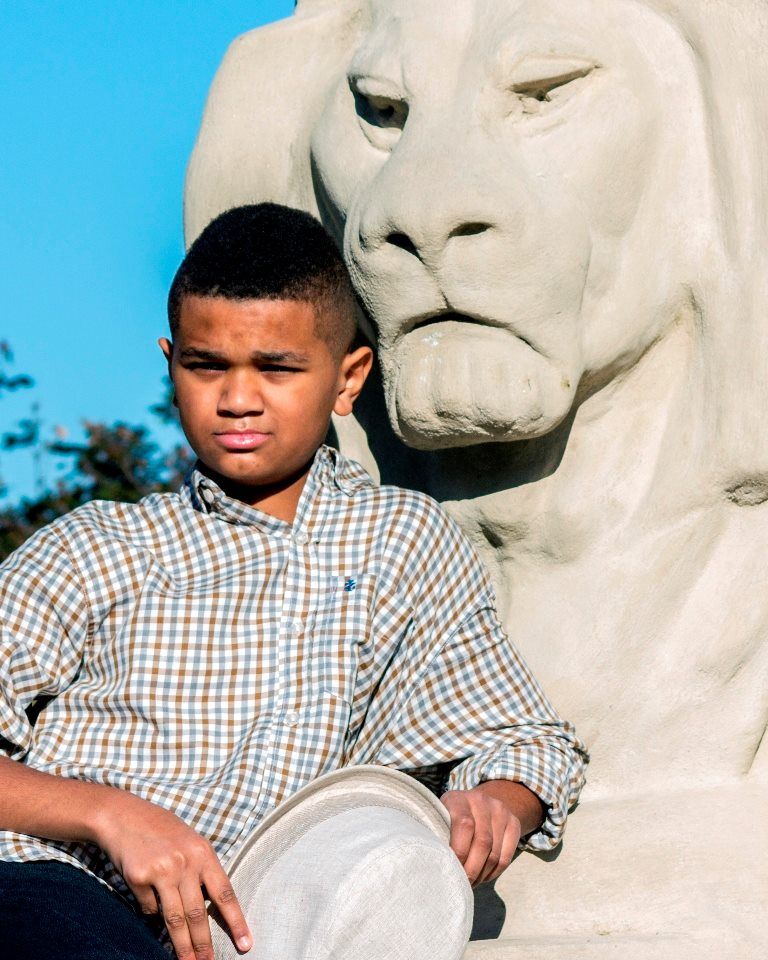 A young boy is sitting in front of a statue of a lion