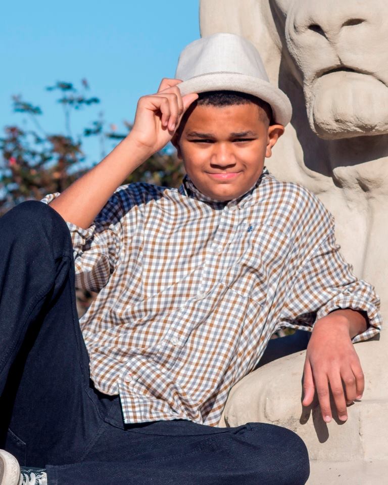 A young boy wearing a hat sits next to a statue of a lion