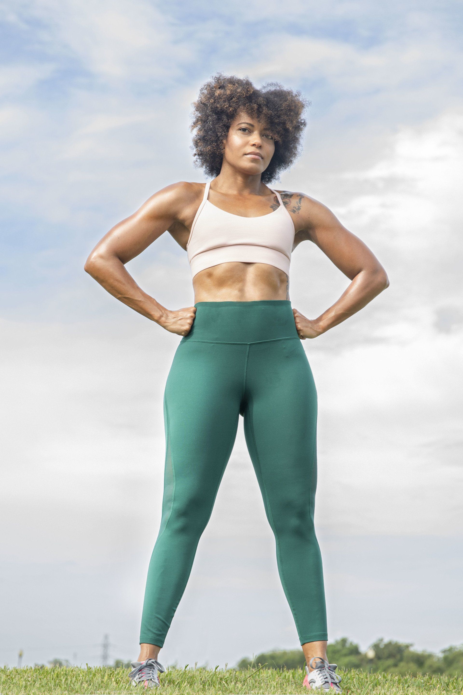 A woman is standing in a field with her hands on her hips.