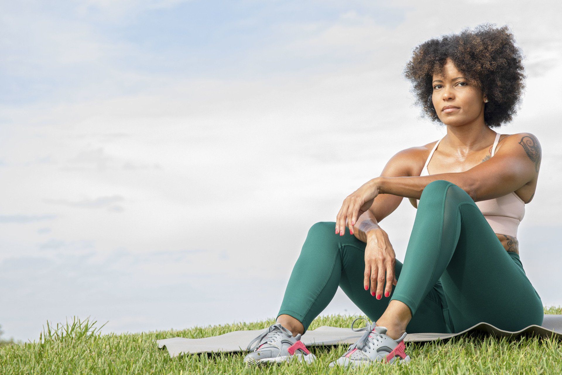 A woman is sitting on a yoga mat in the grass.
