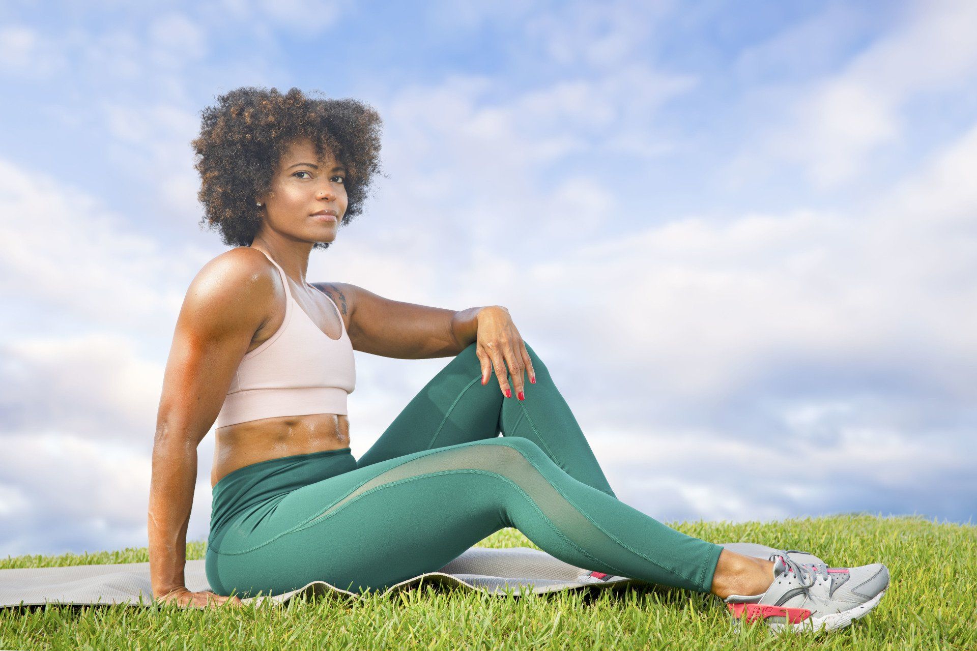 A woman is sitting on a yoga mat in the grass.