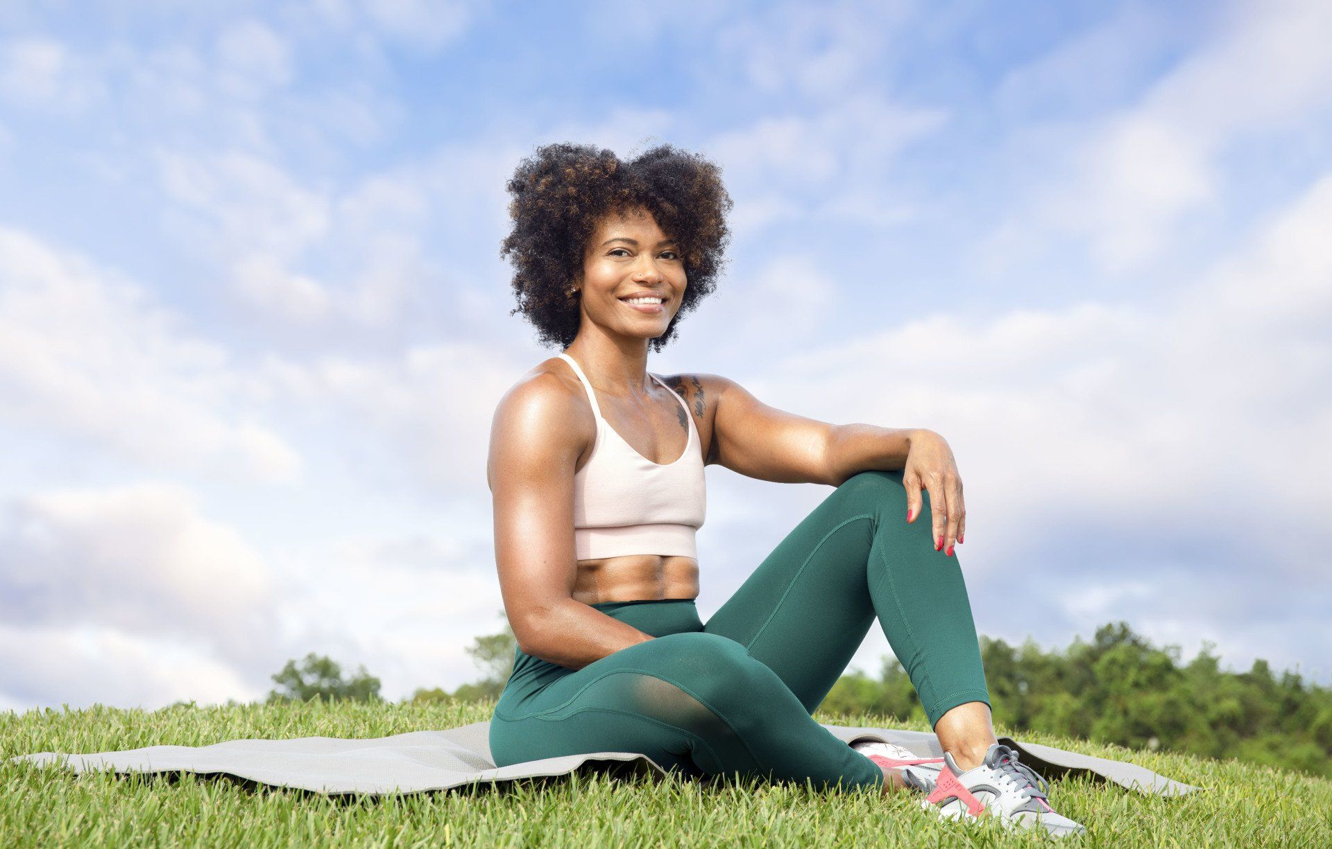 A woman is sitting on a yoga mat in the grass.