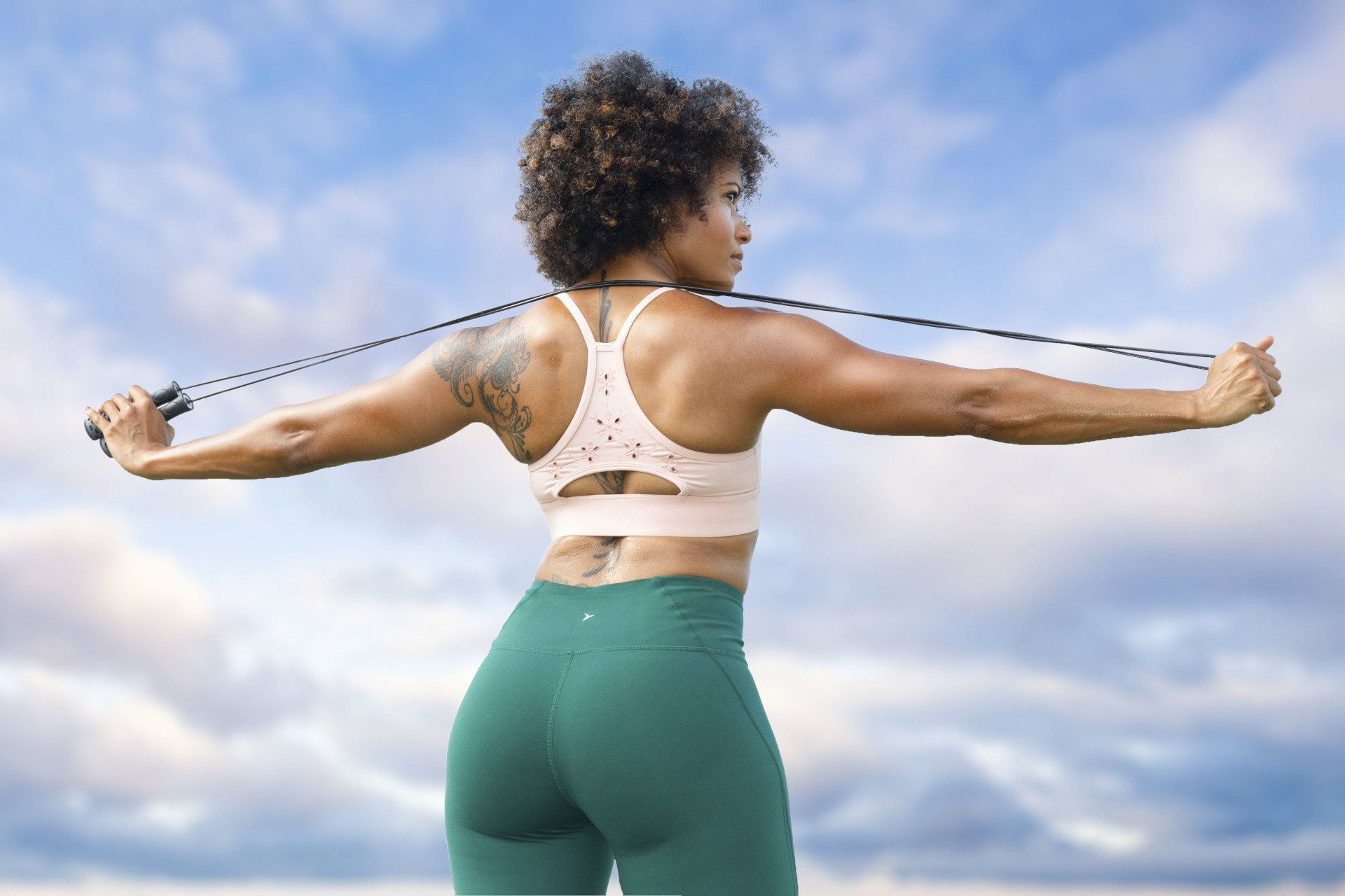 A woman is jumping a jump rope with her arms outstretched.