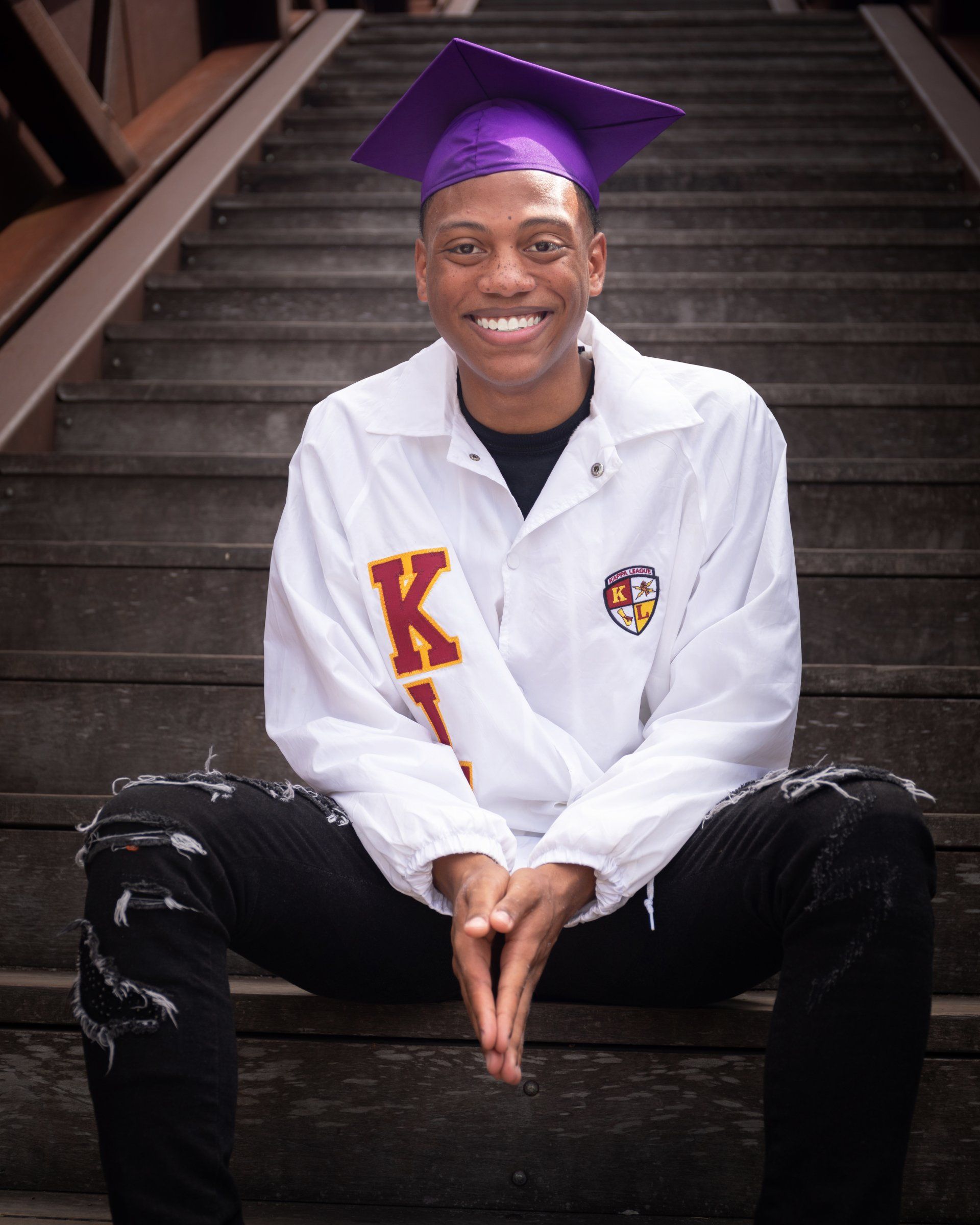 A man wearing a graduation cap and gown is sitting on a set of stairs