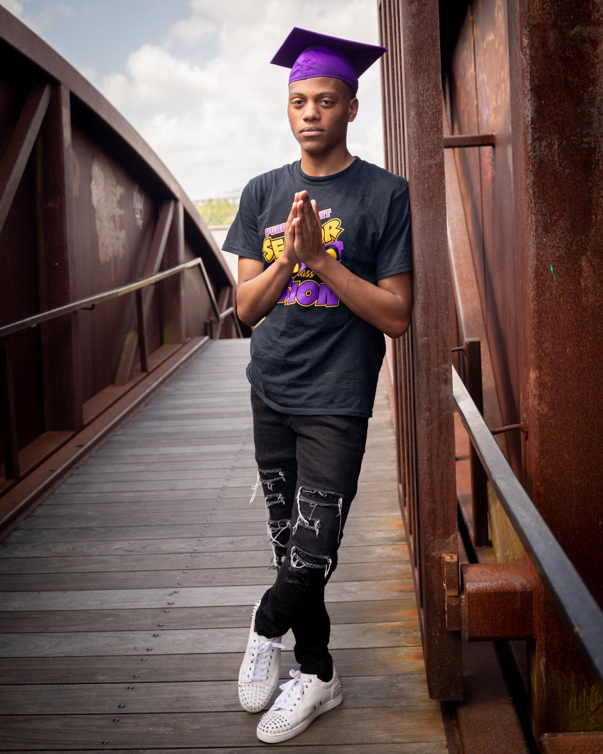 A man wearing a graduation cap and gown is standing on a bridge.