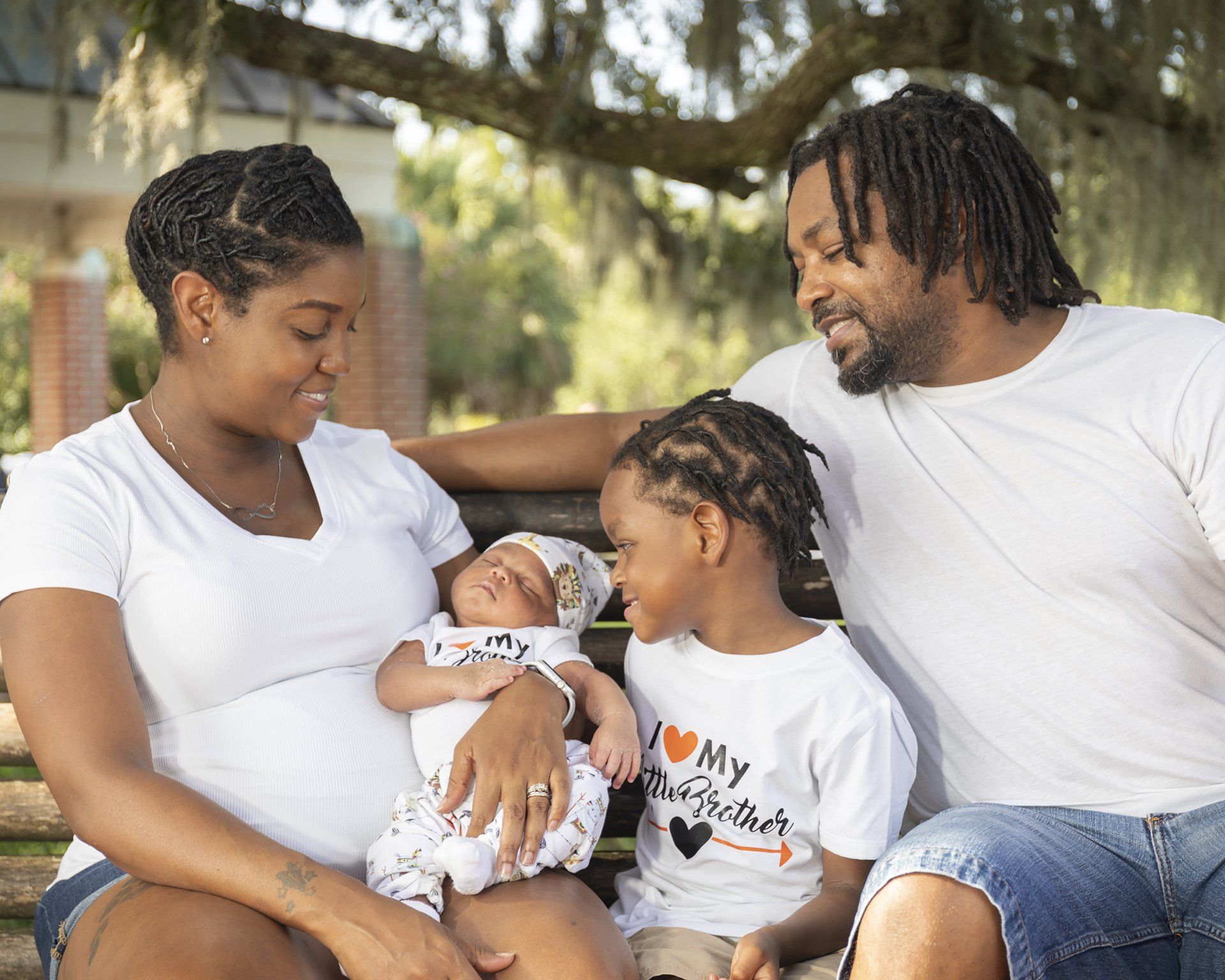 A family is sitting on a bench holding a baby and two children.