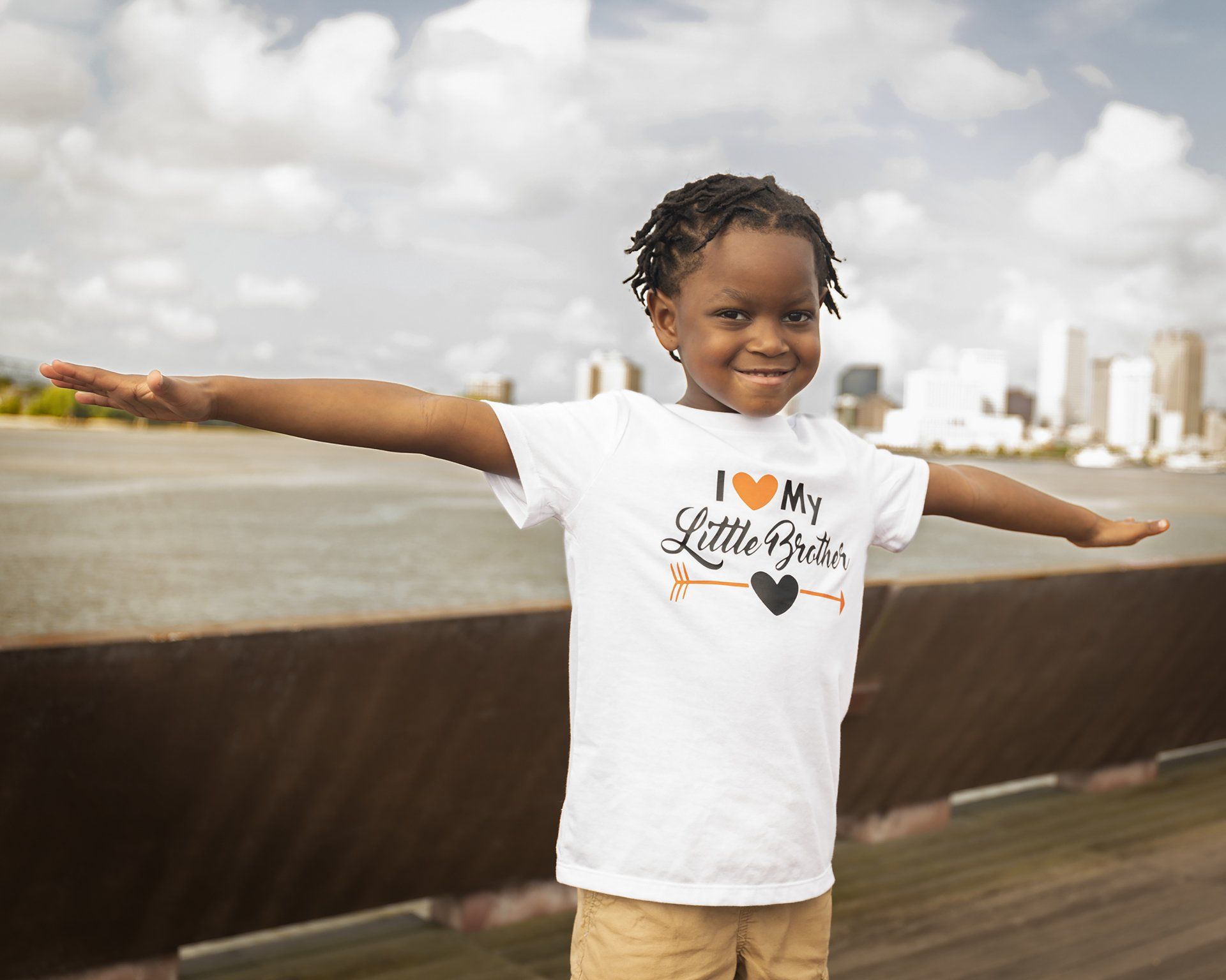 A little girl is standing on a bridge with her arms outstretched.