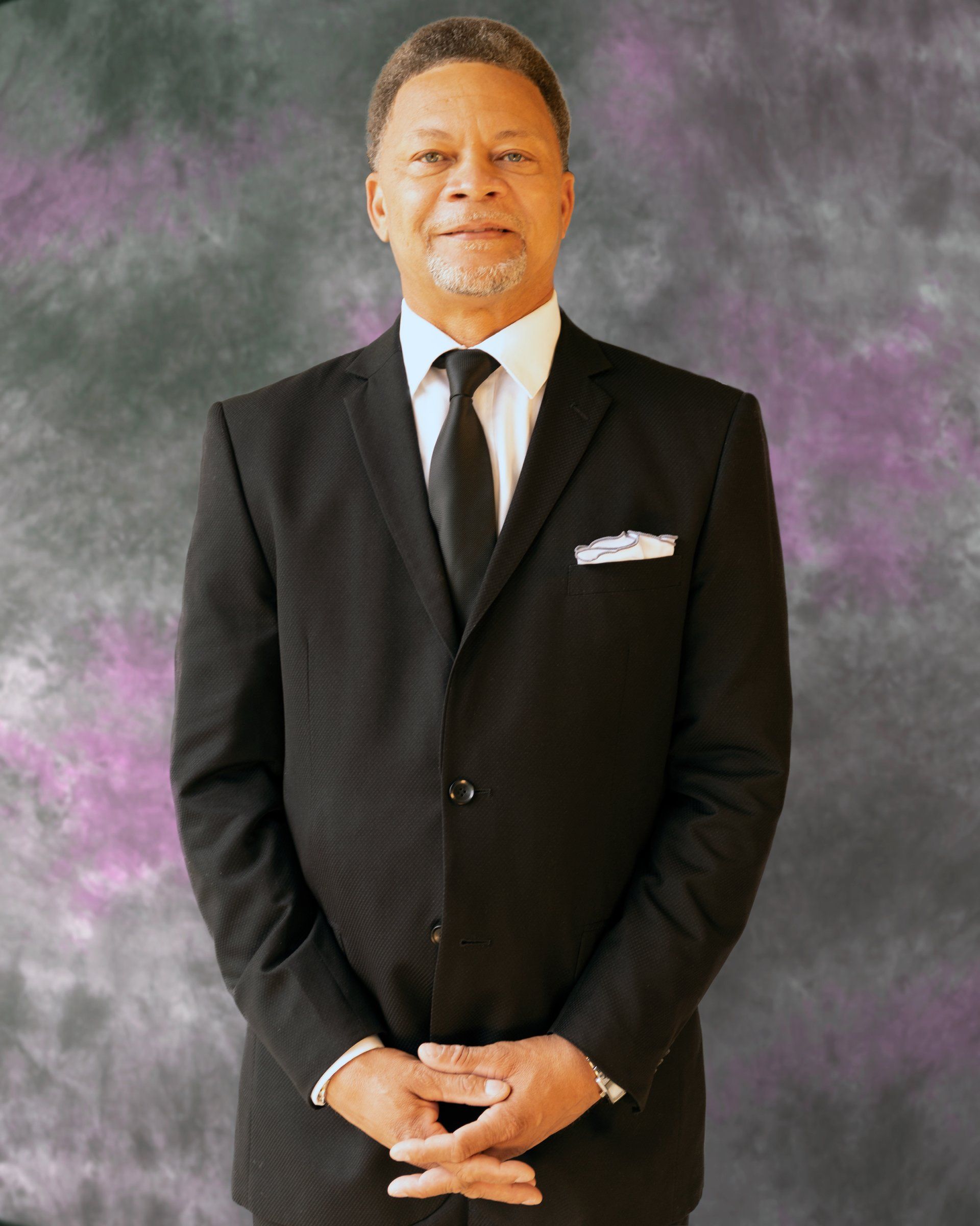 A man in a suit and tie is standing with his hands folded