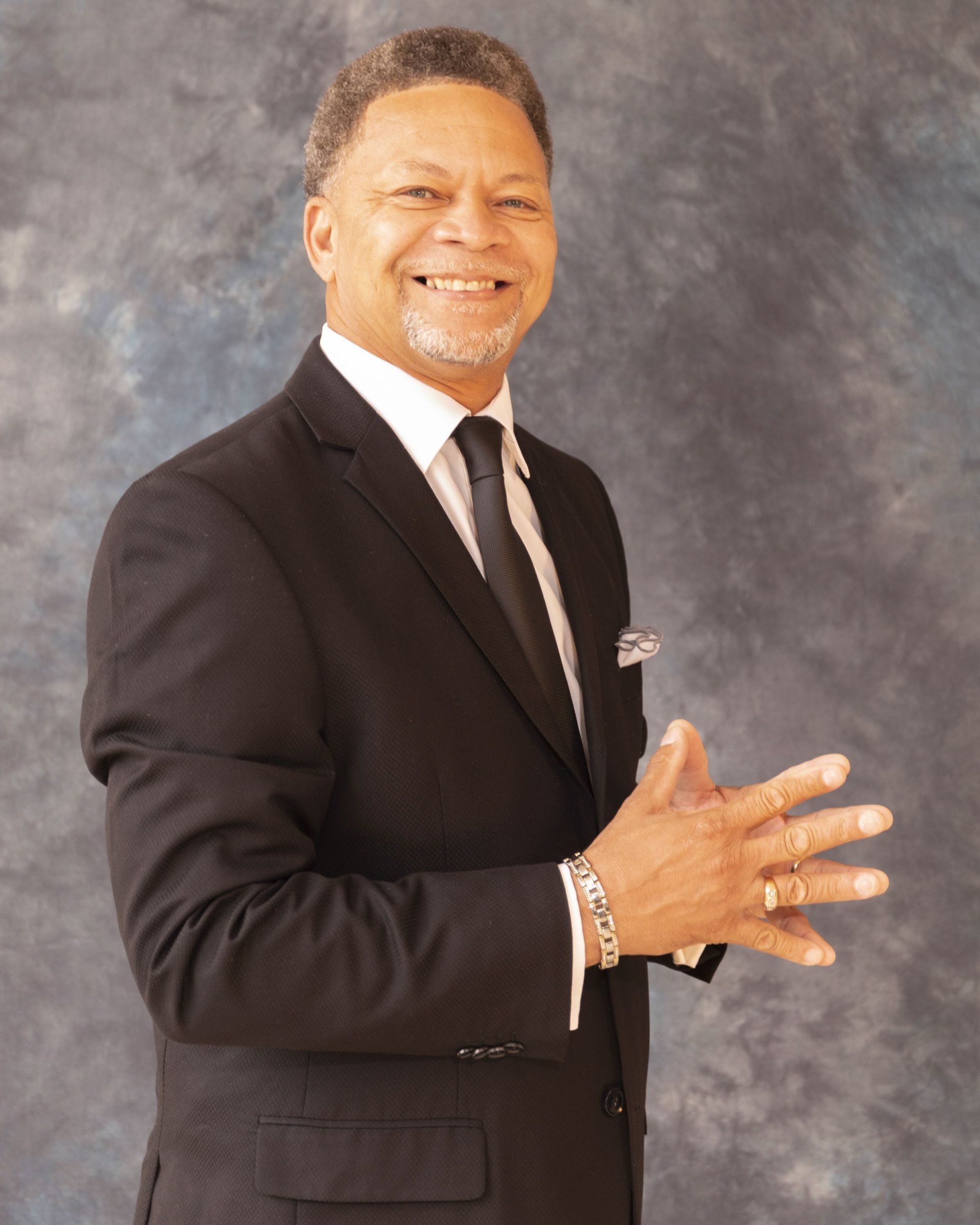 A man in a suit and tie is smiling with his hands folded