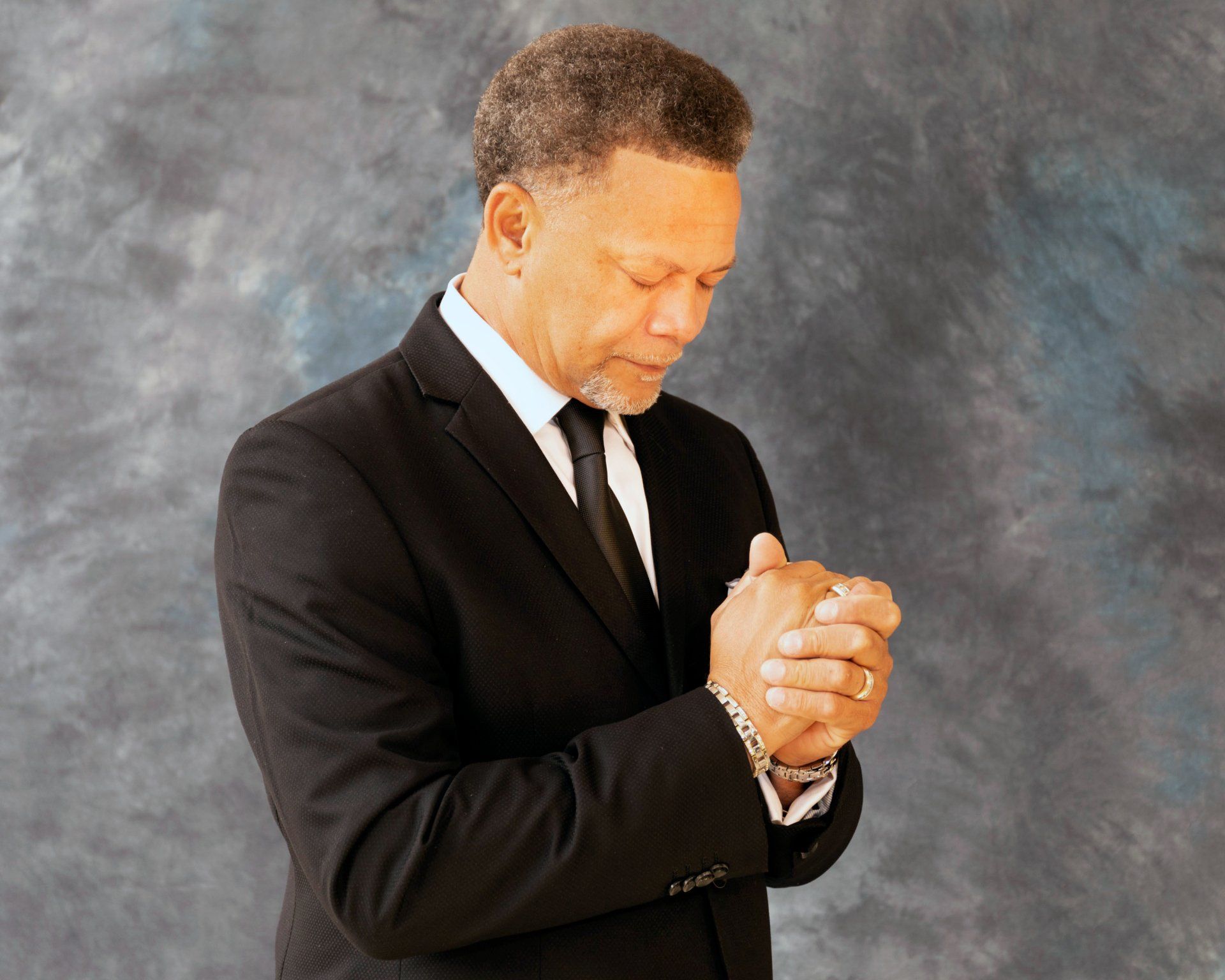A man in a suit and tie is praying with his hands folded