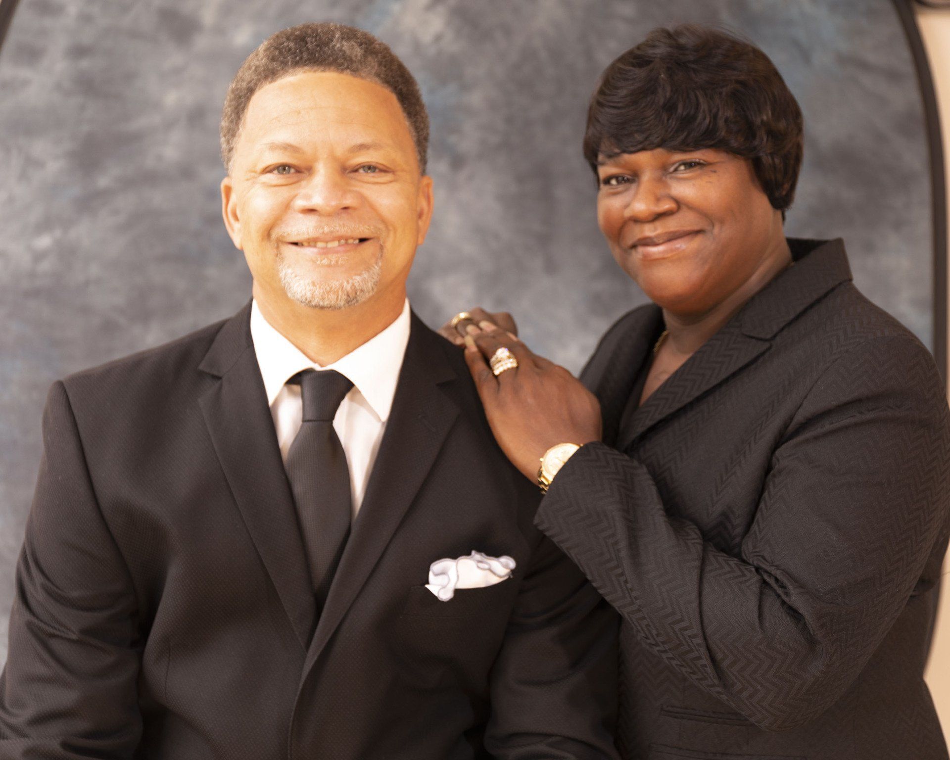 A man and woman are posing for a picture and the woman is putting her hand on the man 's shoulder
