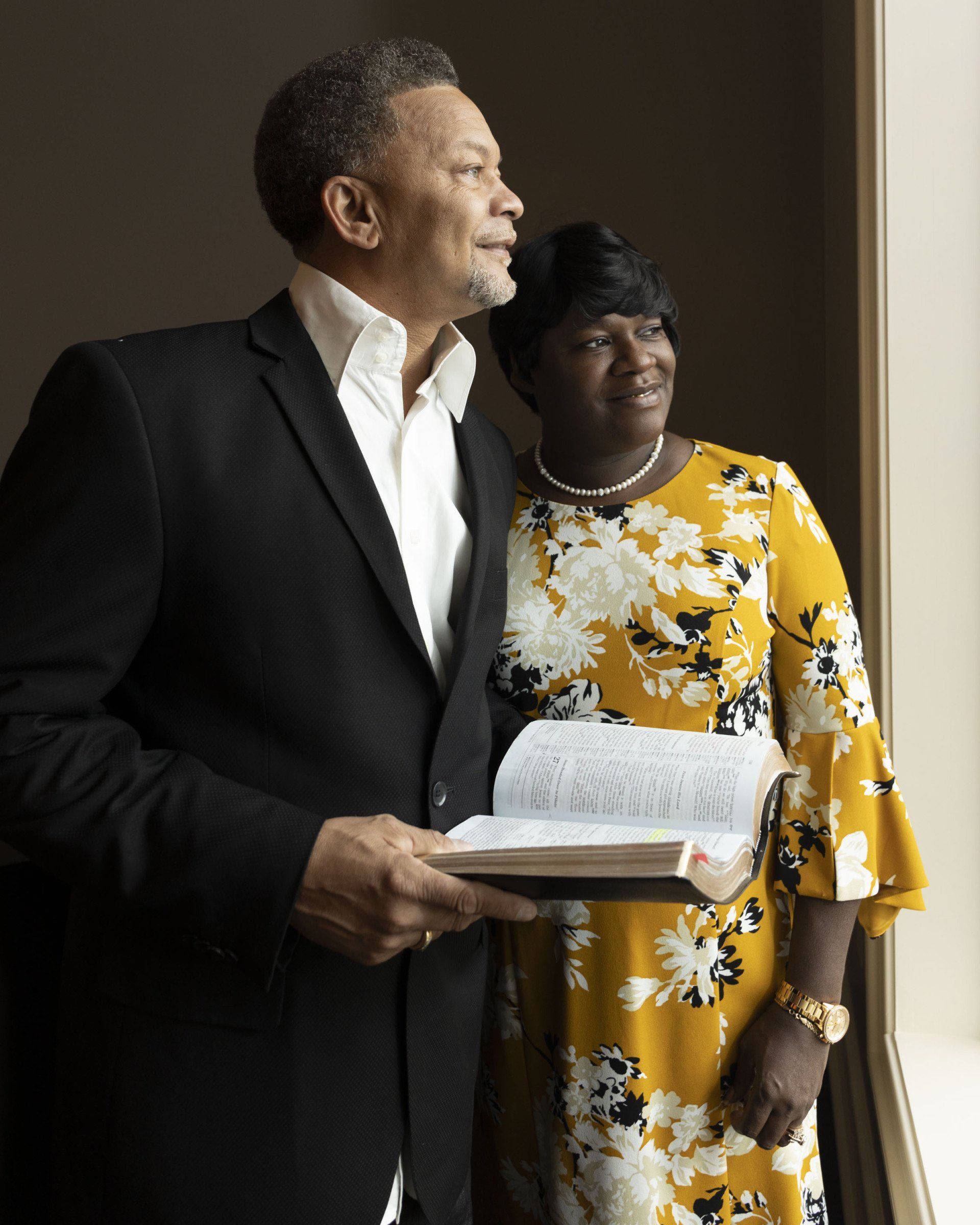 A man in a suit and a woman in a yellow dress are standing next to each other holding a bible.