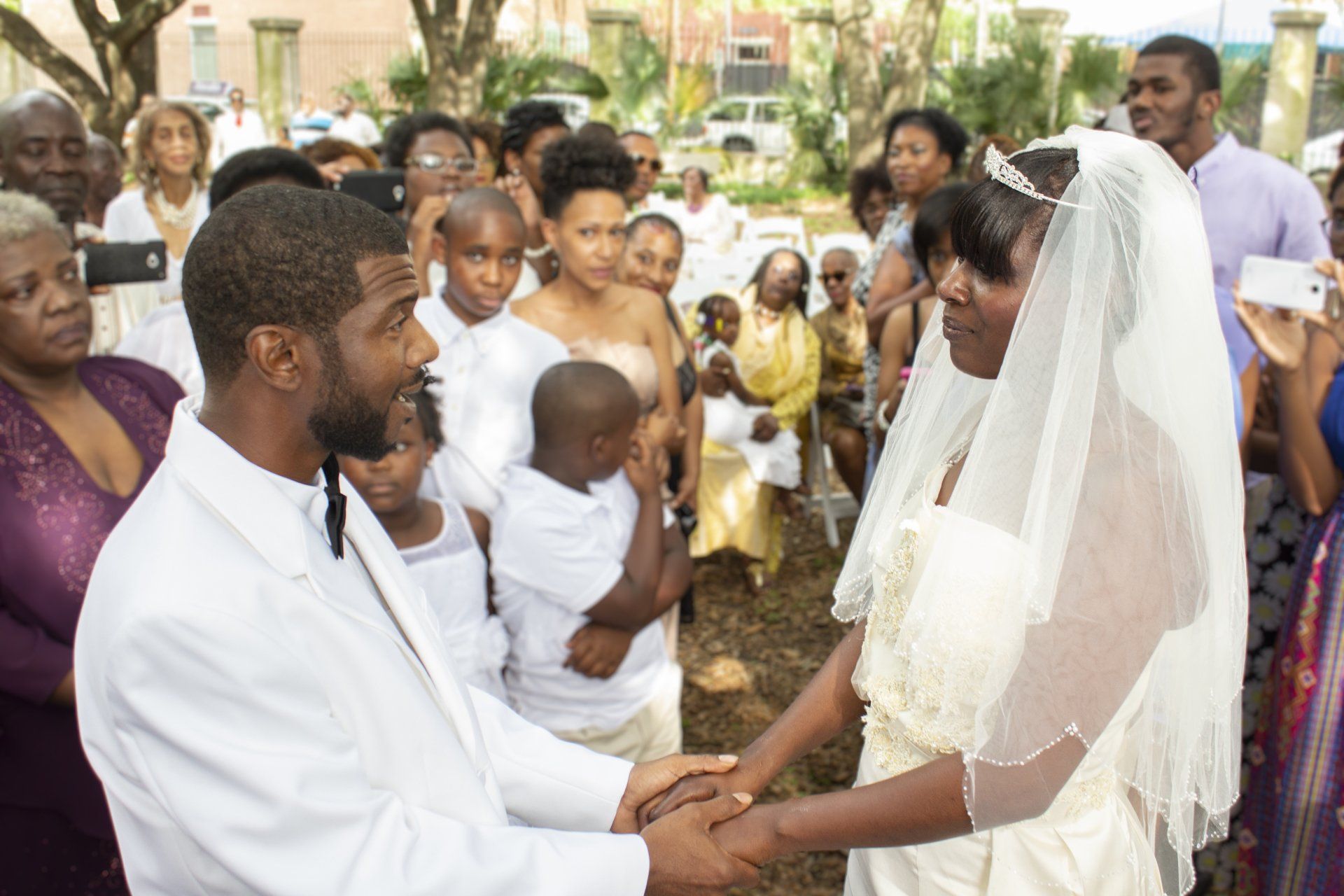 A bride and groom are shaking hands in front of a crowd of people.