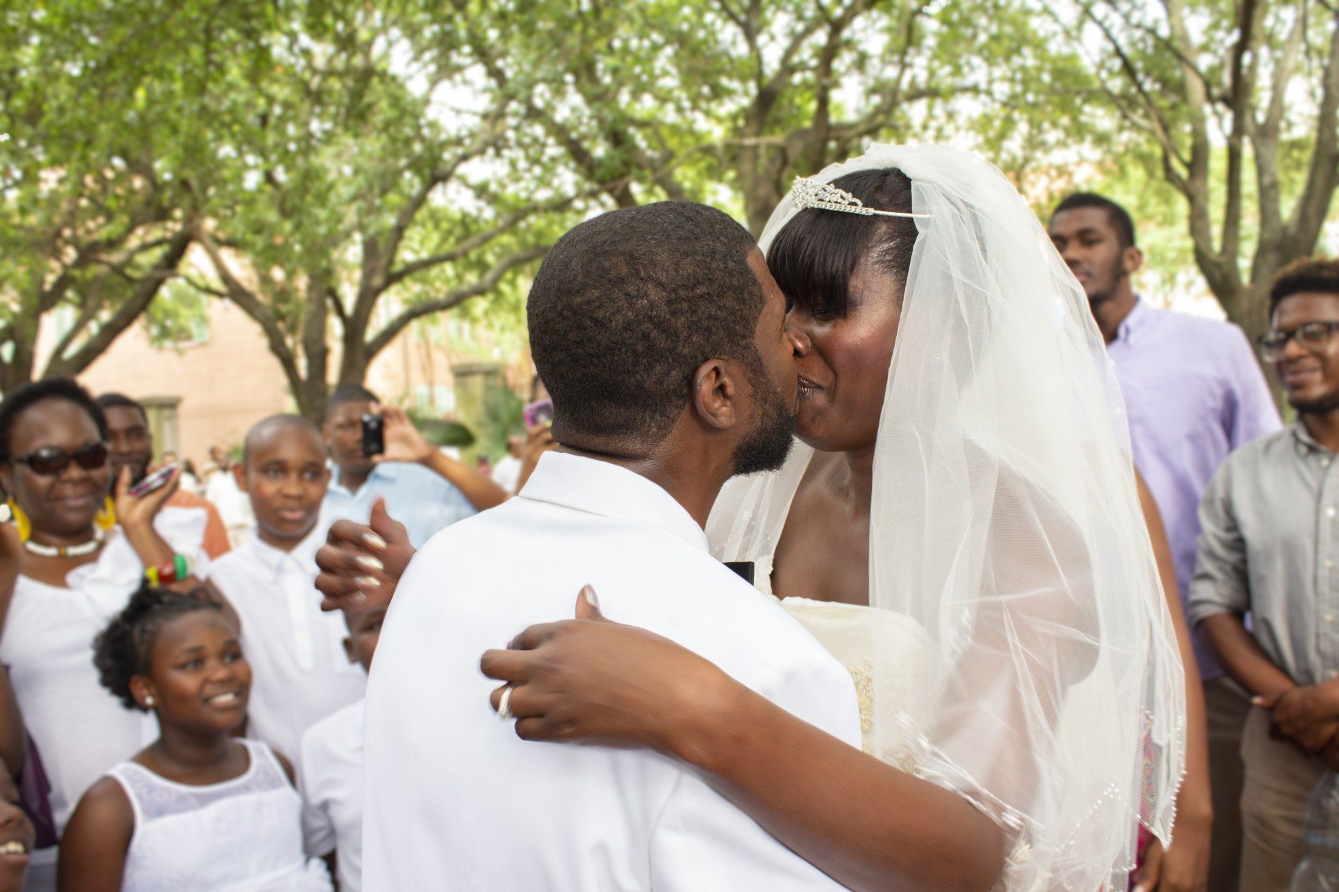 A bride and groom are kissing in front of their wedding guests.