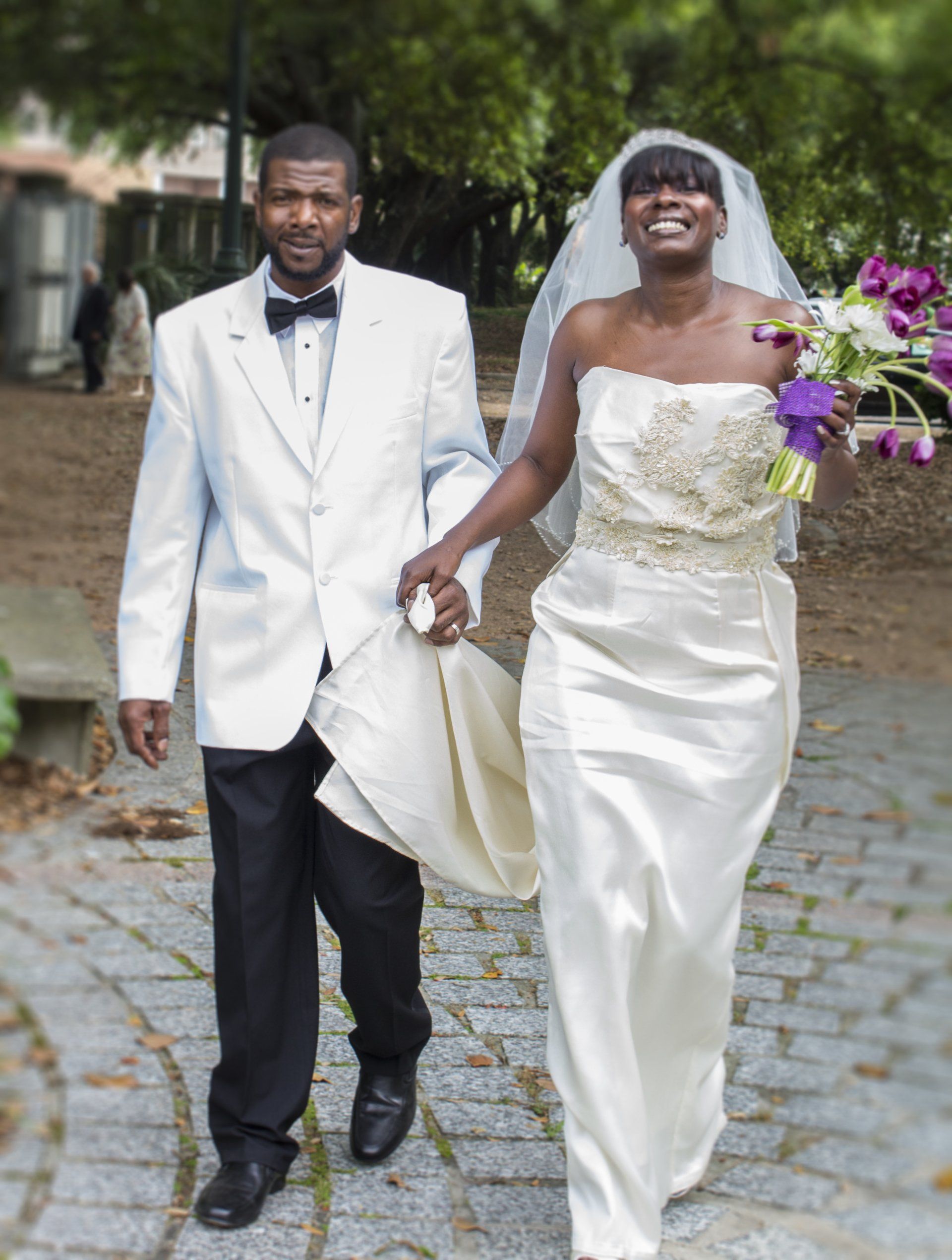 A bride and groom are walking down a sidewalk holding hands