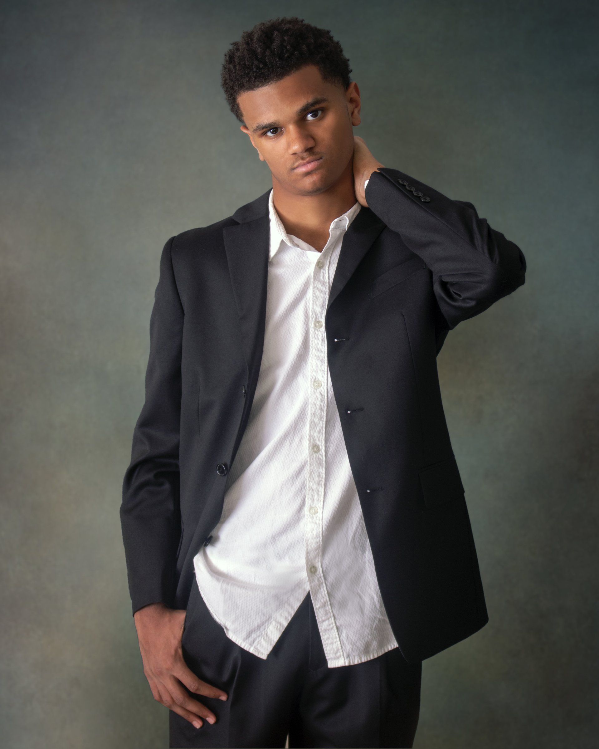 A young man in a suit and white shirt holds his hand to his neck