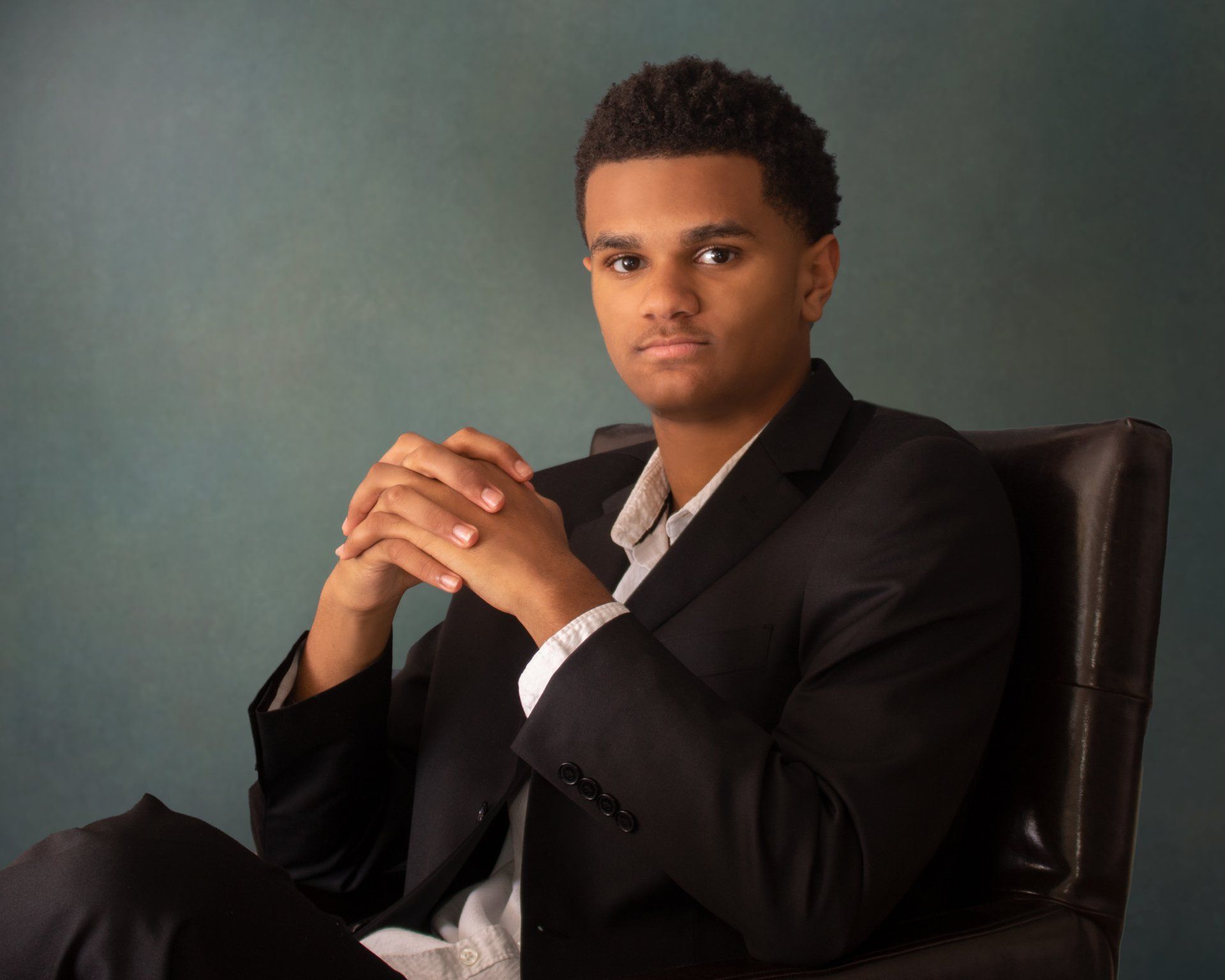 A man in a suit is sitting in a chair with his hands folded