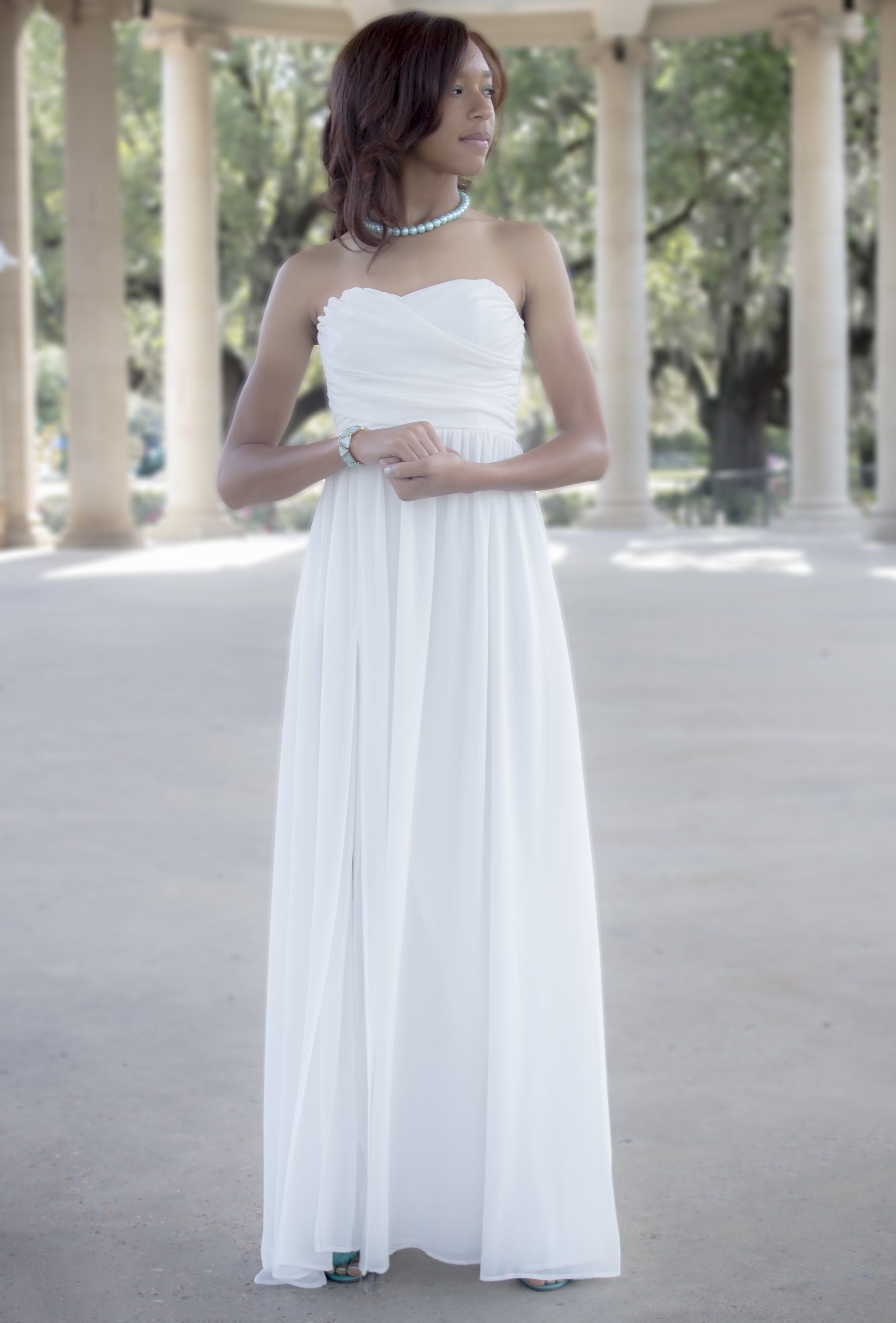 A woman in a white dress is standing in front of columns.