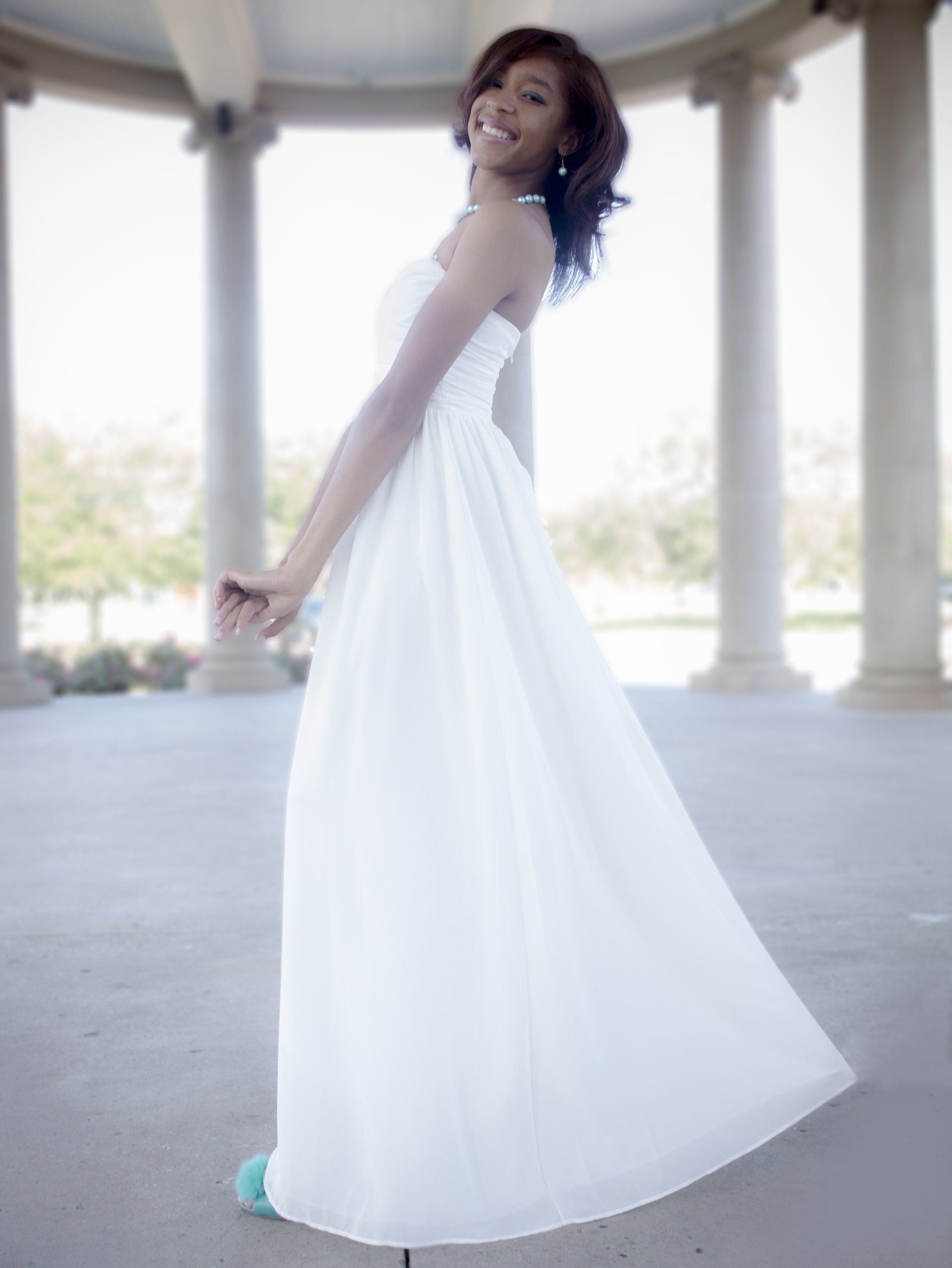 A woman in a white dress is standing in front of columns.