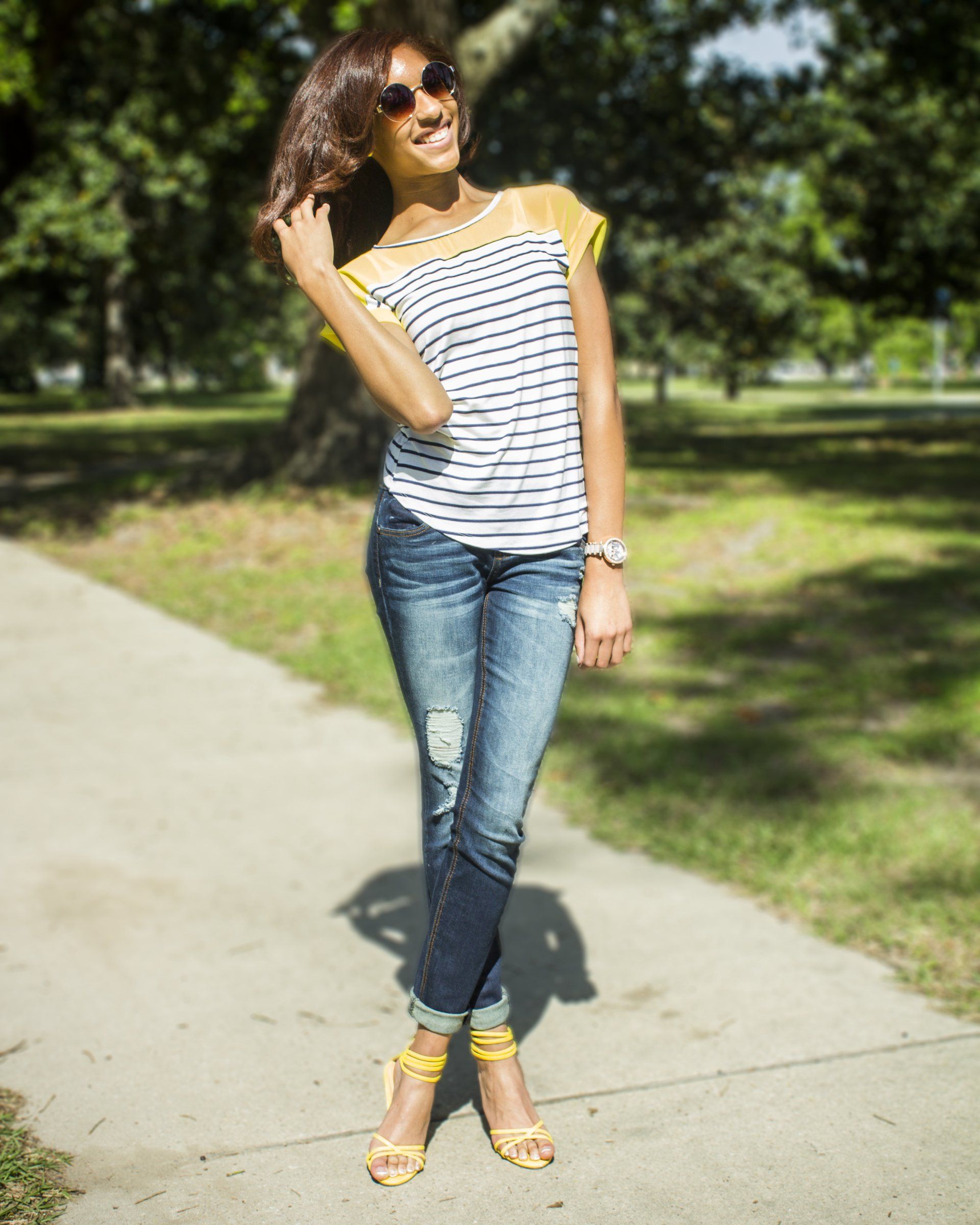 A woman wearing a striped shirt and jeans is standing on a sidewalk.