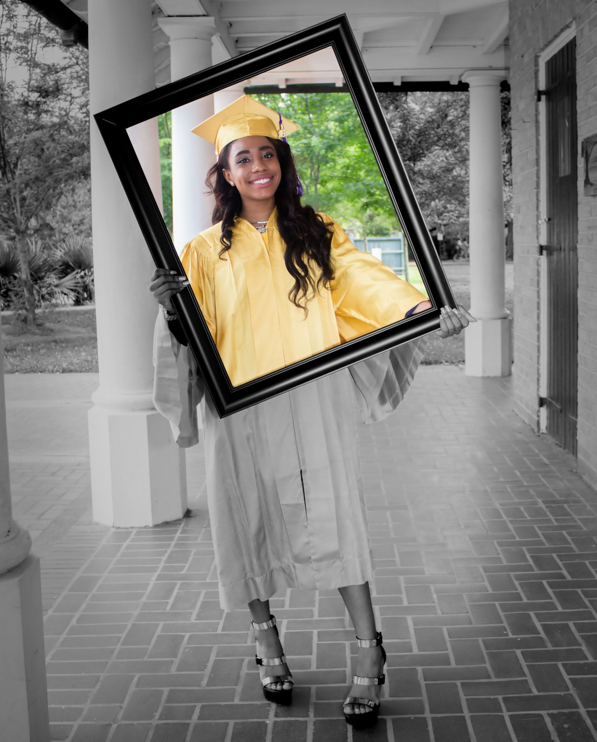 A woman in a yellow cap and gown is holding a picture frame