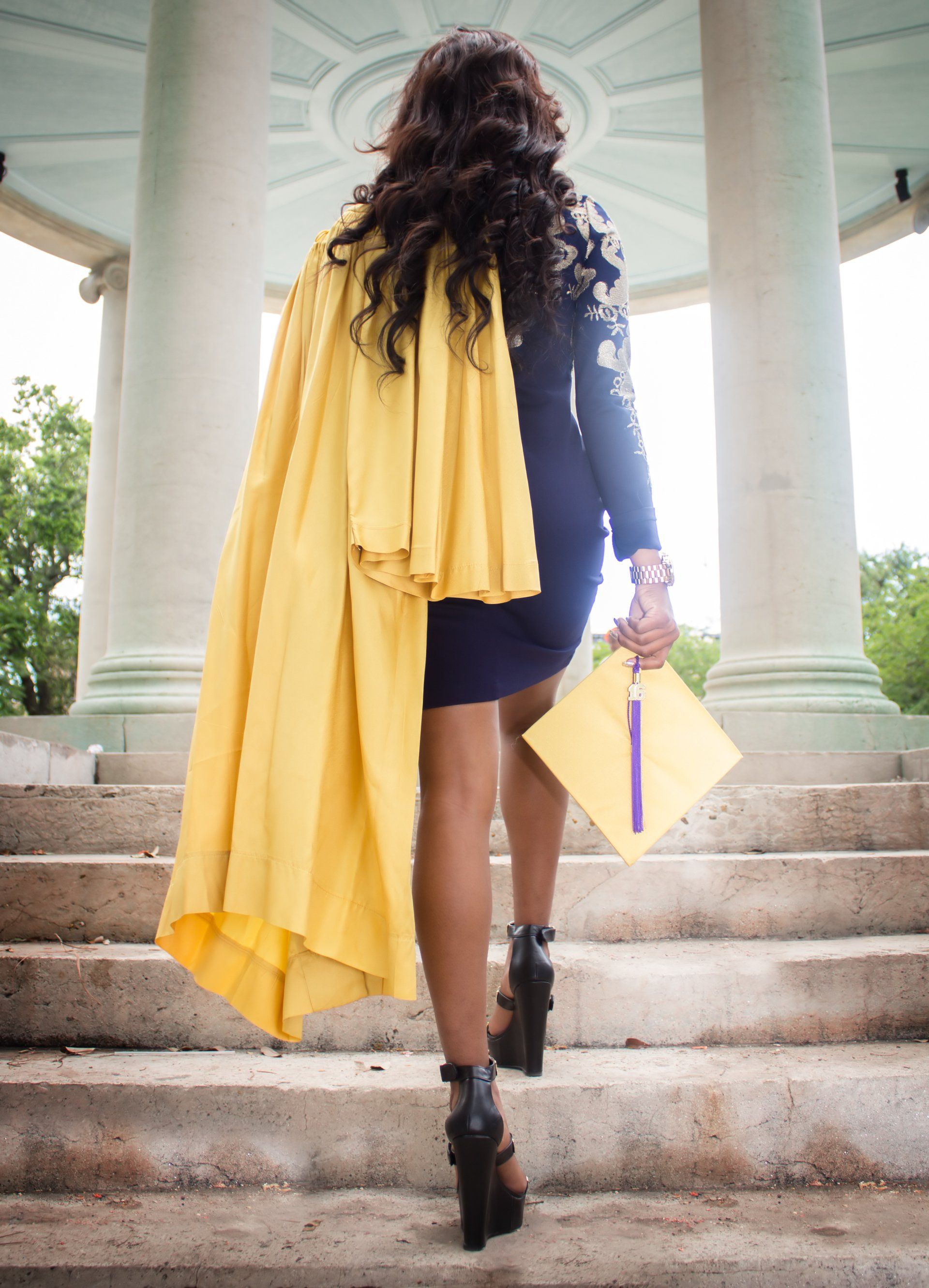 The woman is wearing a cape and holding a graduation cap.