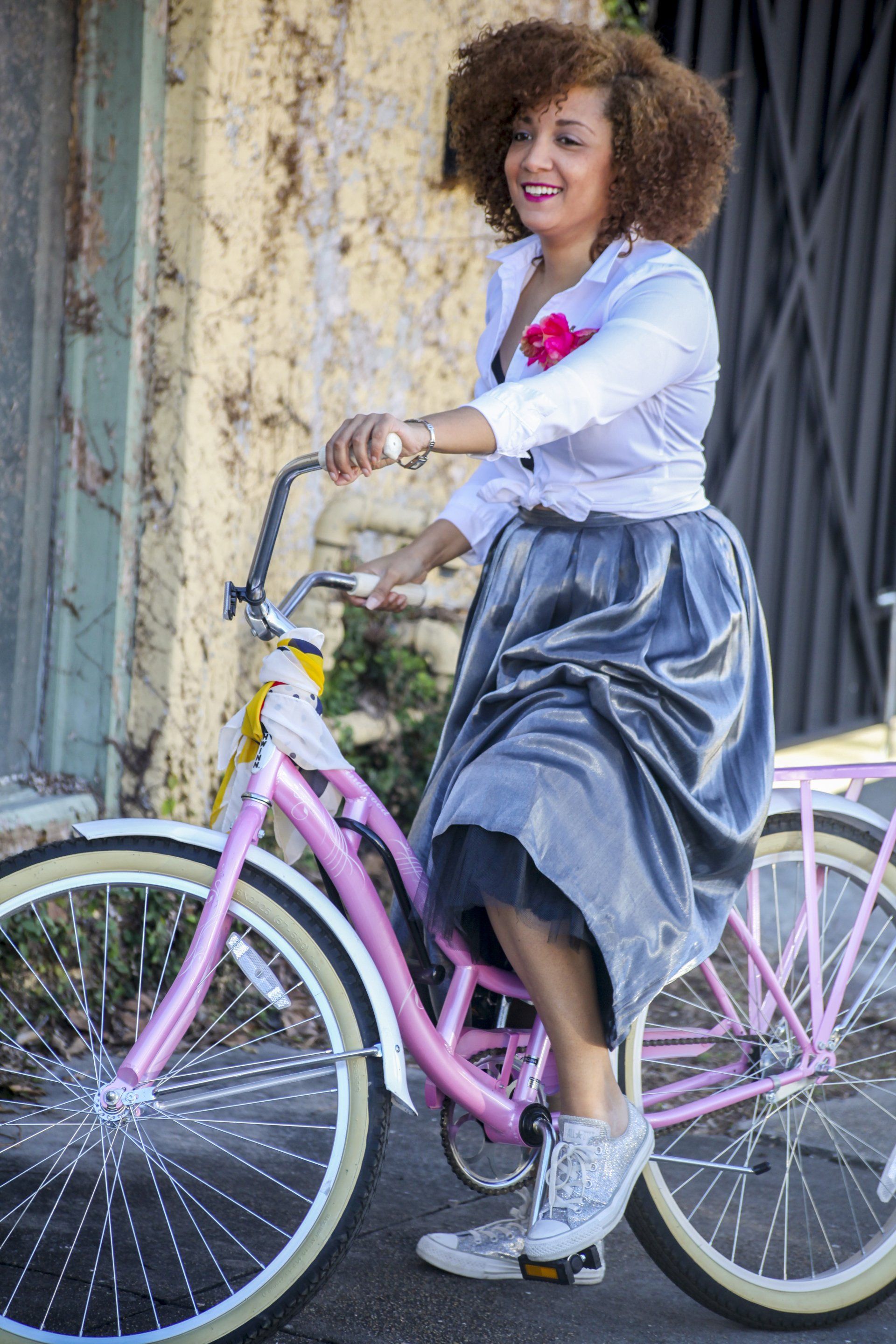 A woman in a skirt is riding a pink bicycle.