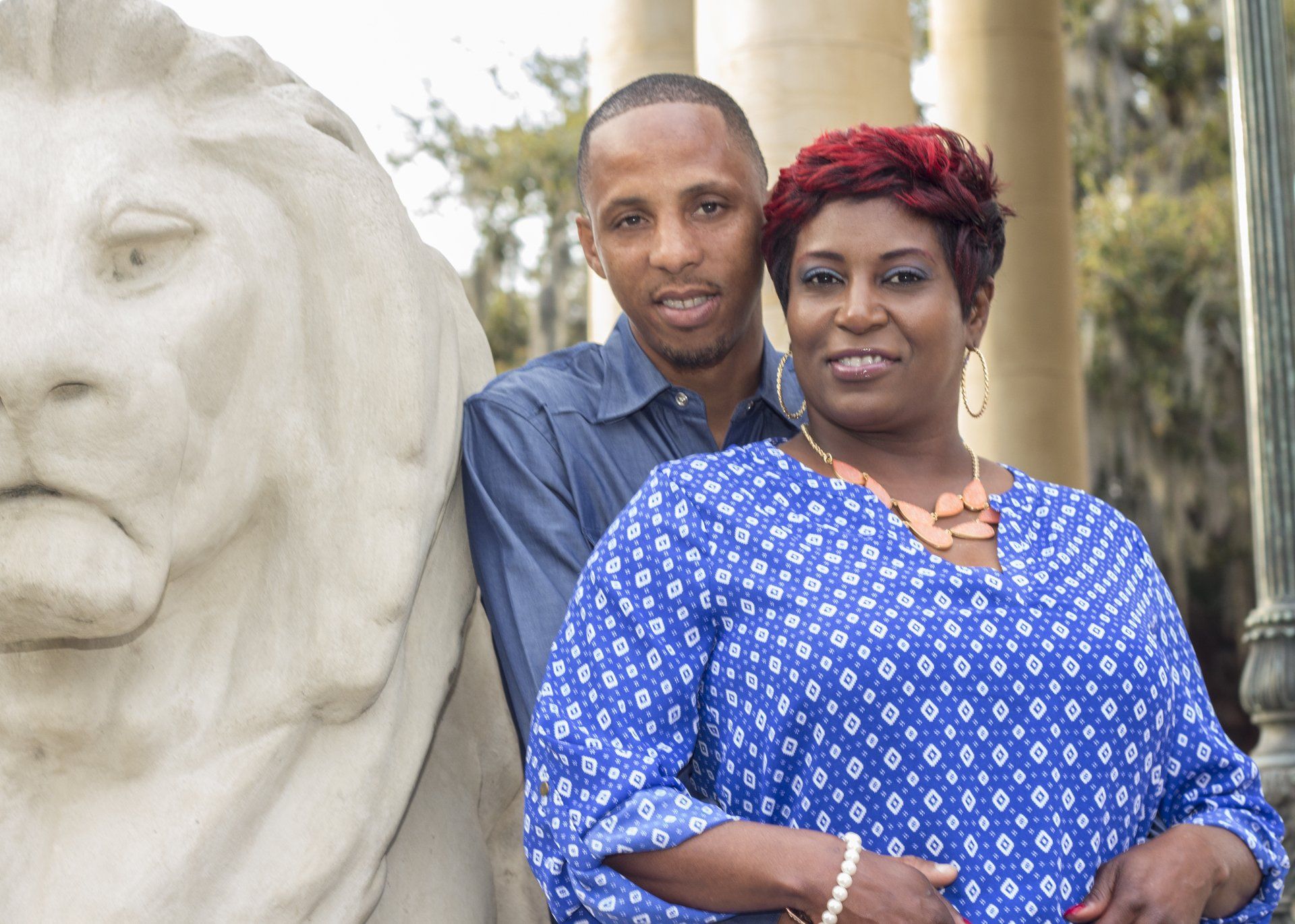 A man and a woman are posing for a picture in front of a statue of a lion.