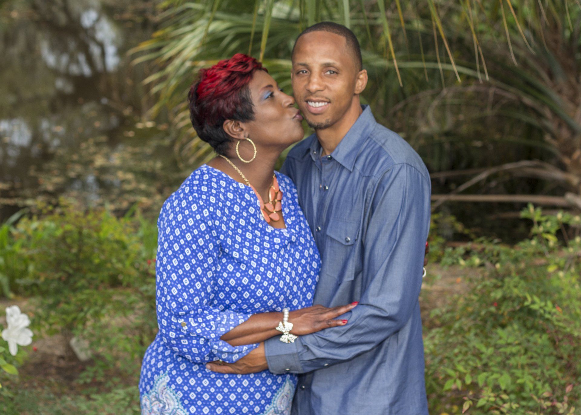 A woman is kissing a man on the cheek in a park.