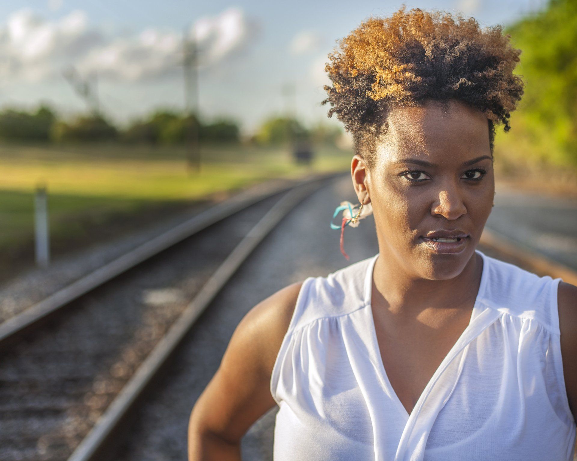 A woman in a white shirt is standing on train tracks.