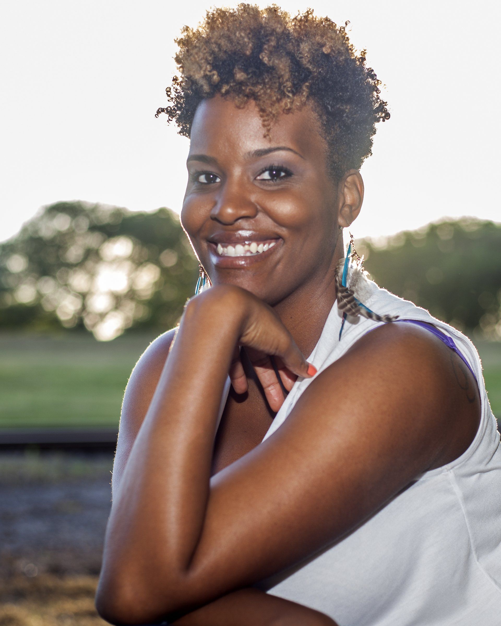 A woman with curly hair is smiling with her hand on her chin