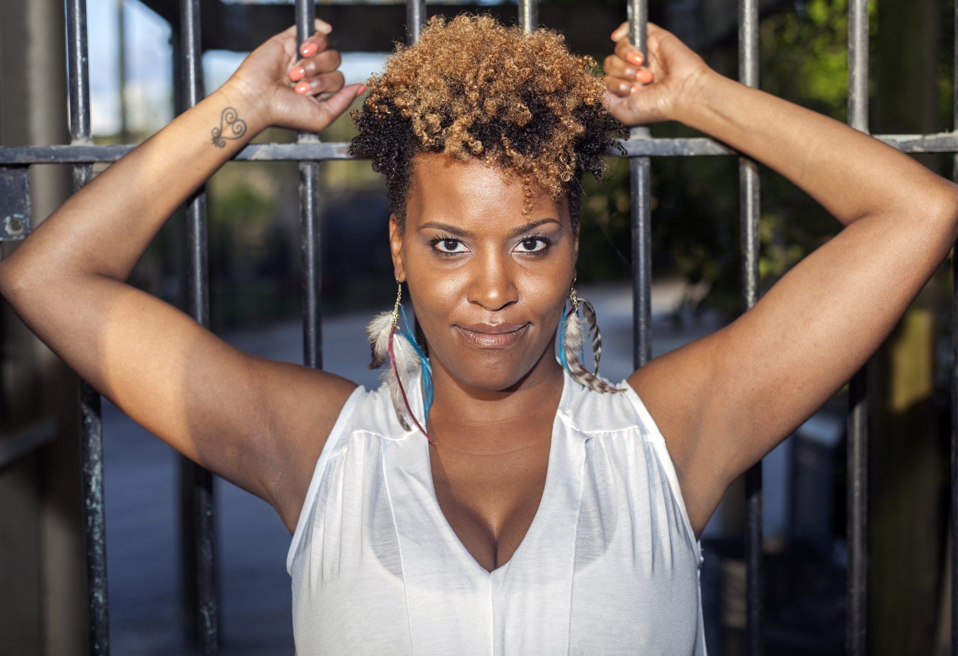 A woman in a white tank top is standing in front of a fence