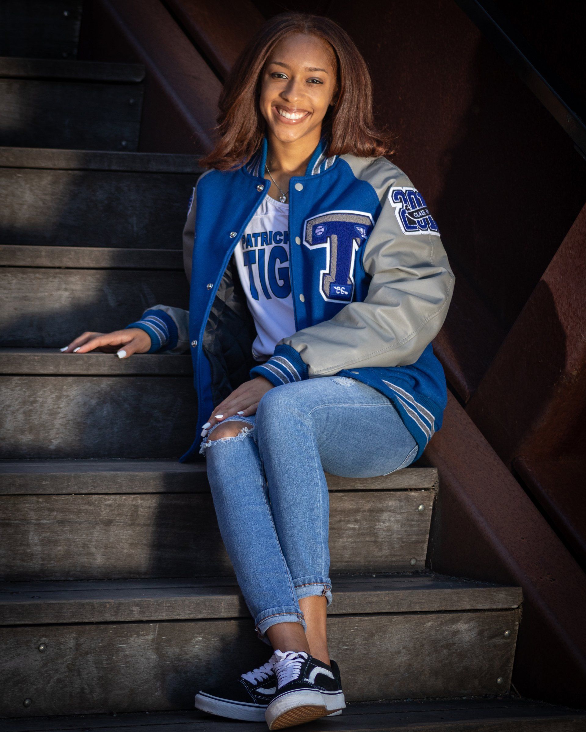 A woman wearing a letterman jacket is sitting on a set of stairs.