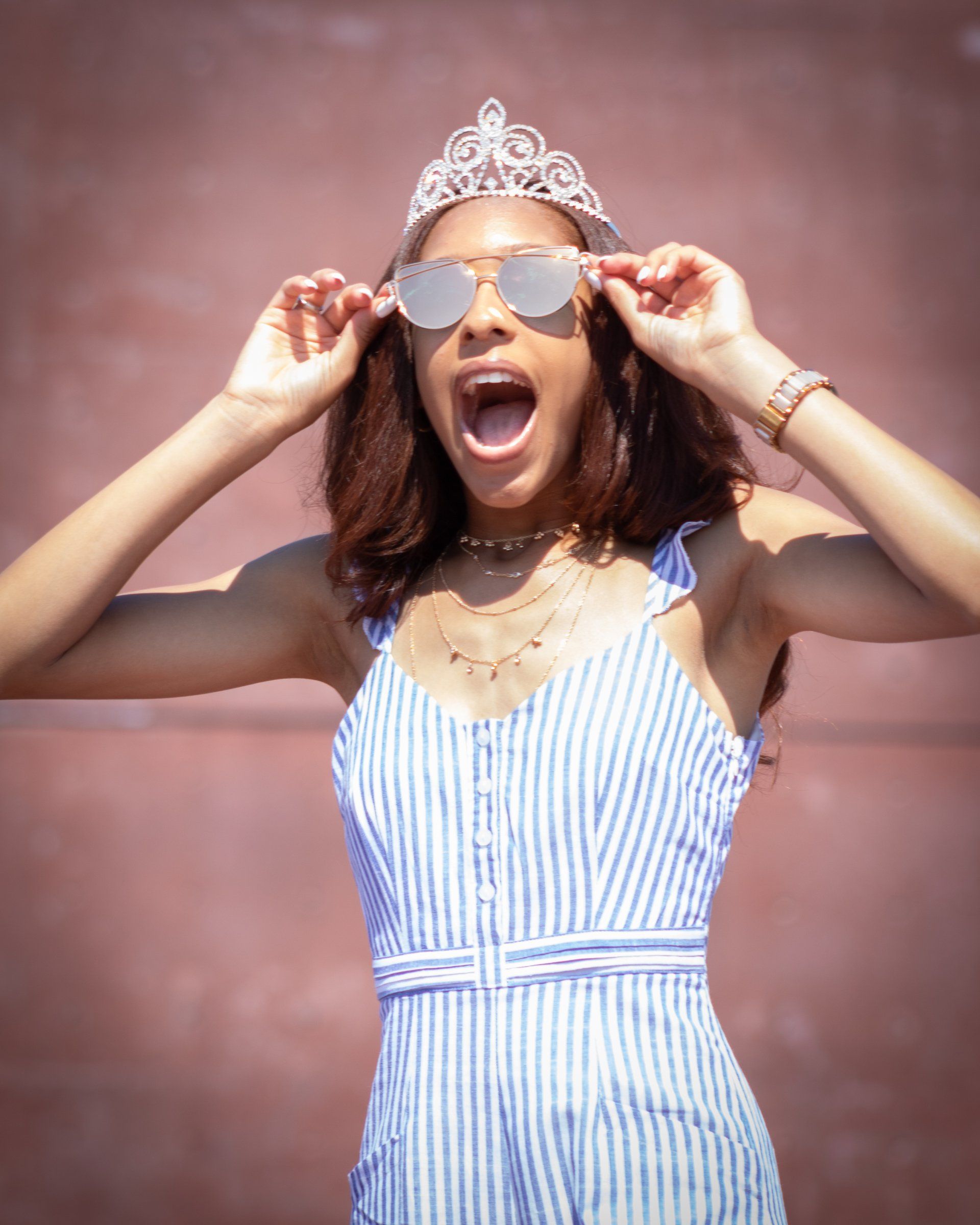 A woman wearing a tiara and sunglasses is making a funny face