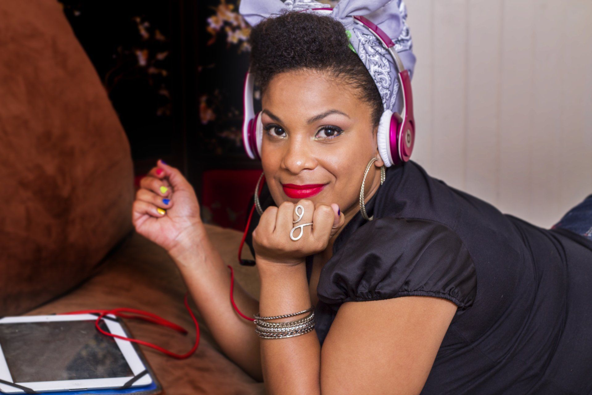 A woman wearing headphones is laying on the floor next to a tablet.