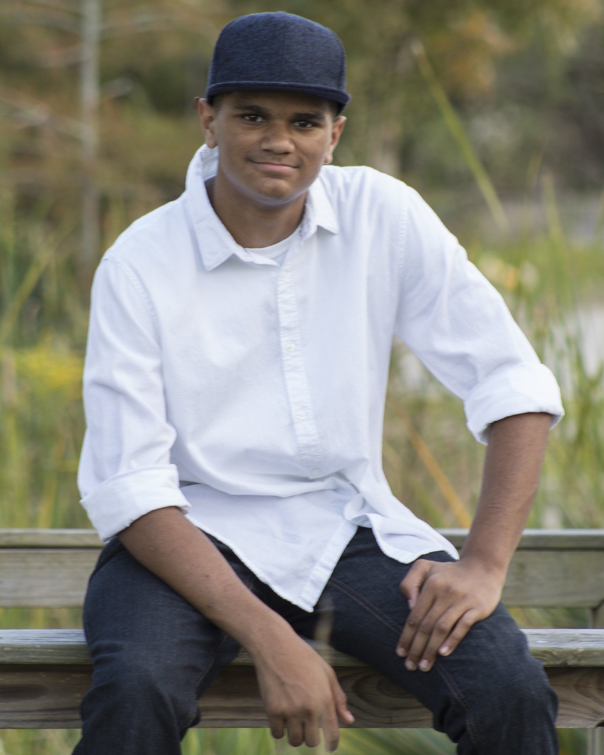 A man wearing a white shirt and a black hat is sitting on a wooden bench.