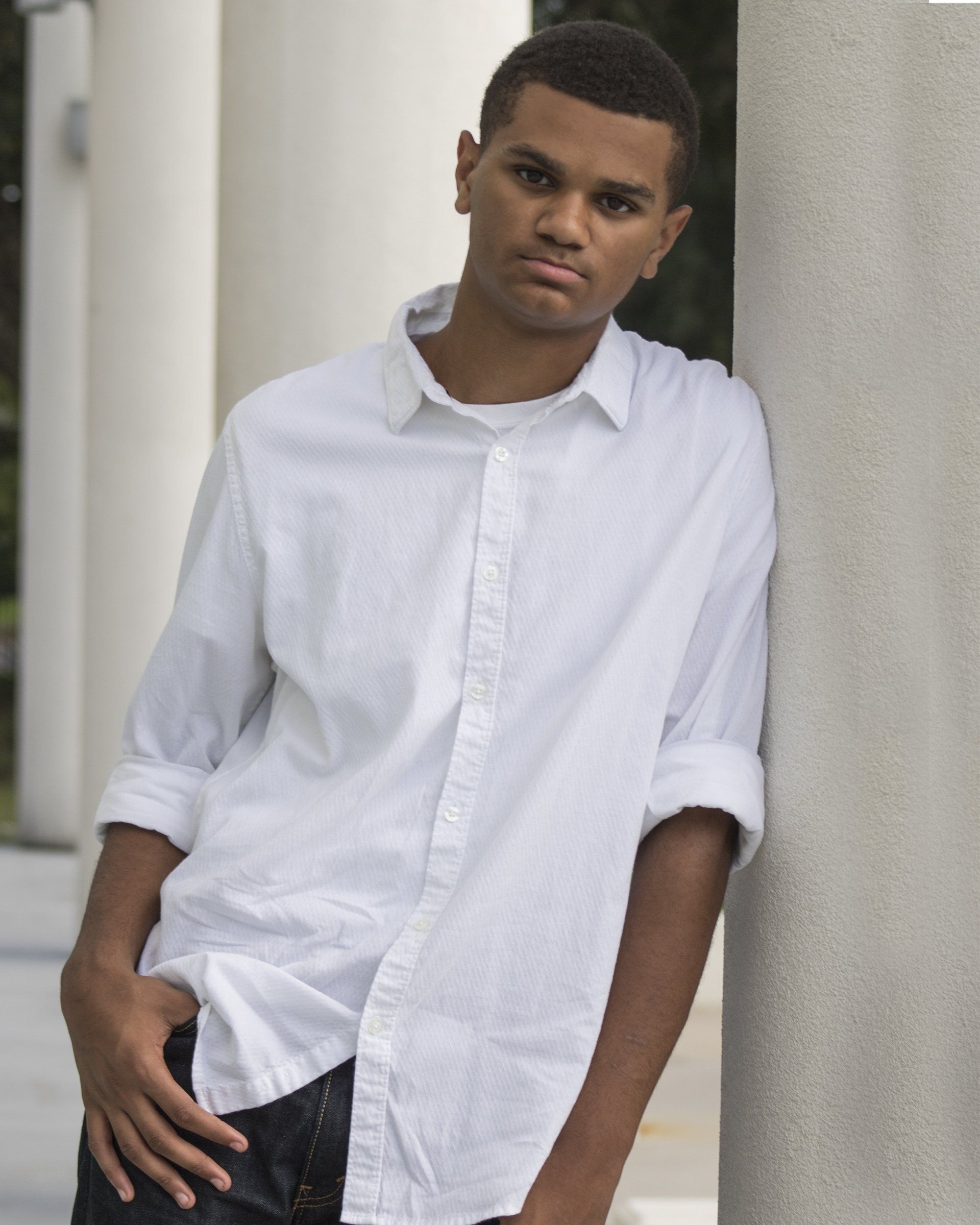 A man in a white shirt leans against a pillar