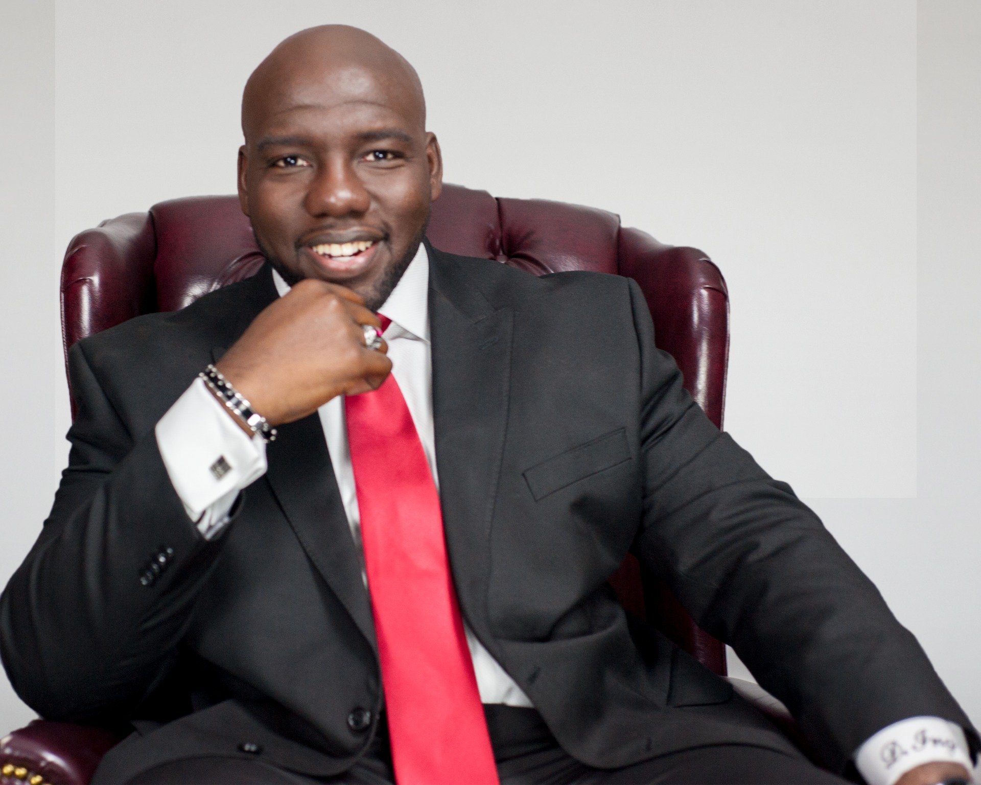 A man in a suit and red tie is sitting in a chair