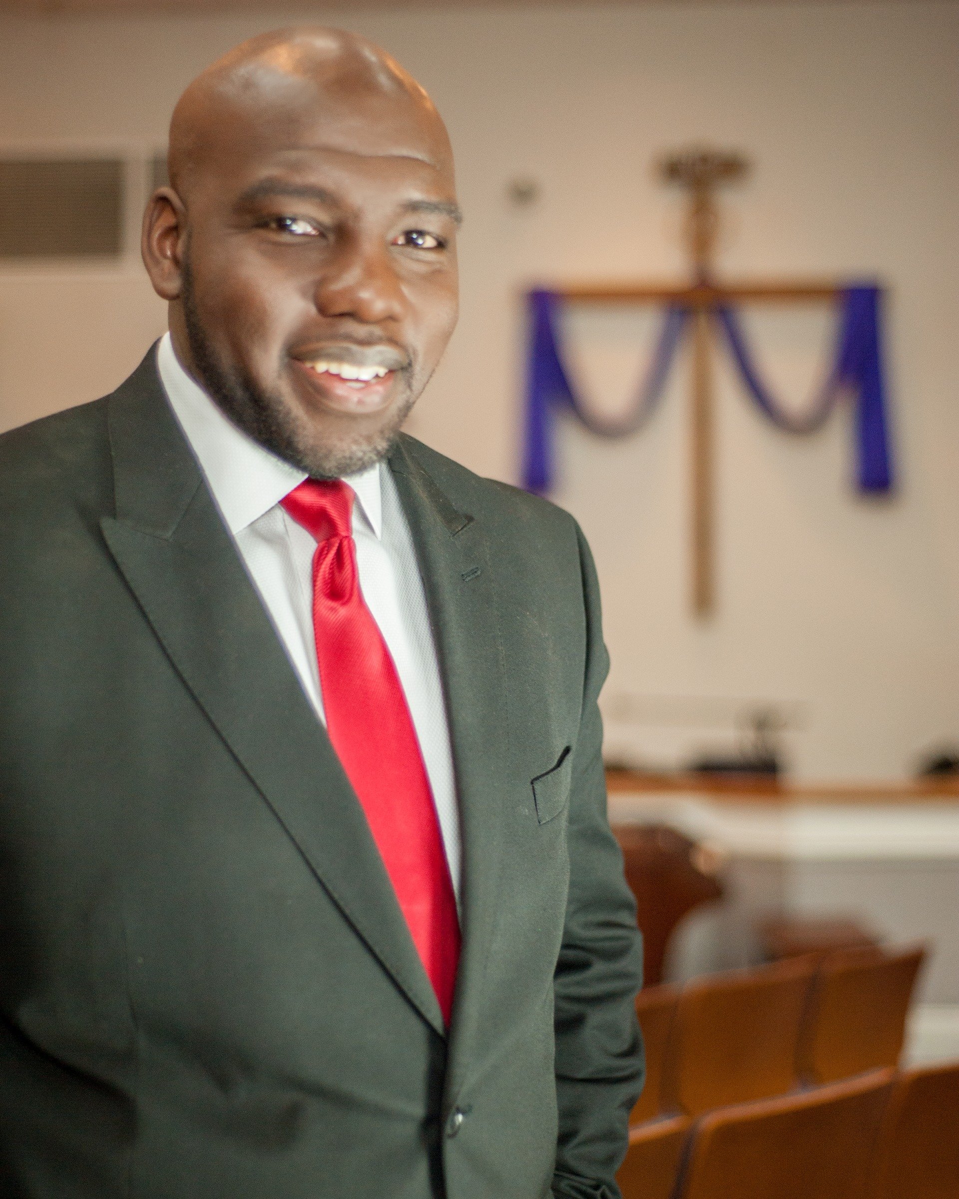 A man in a suit and tie stands in front of a cross