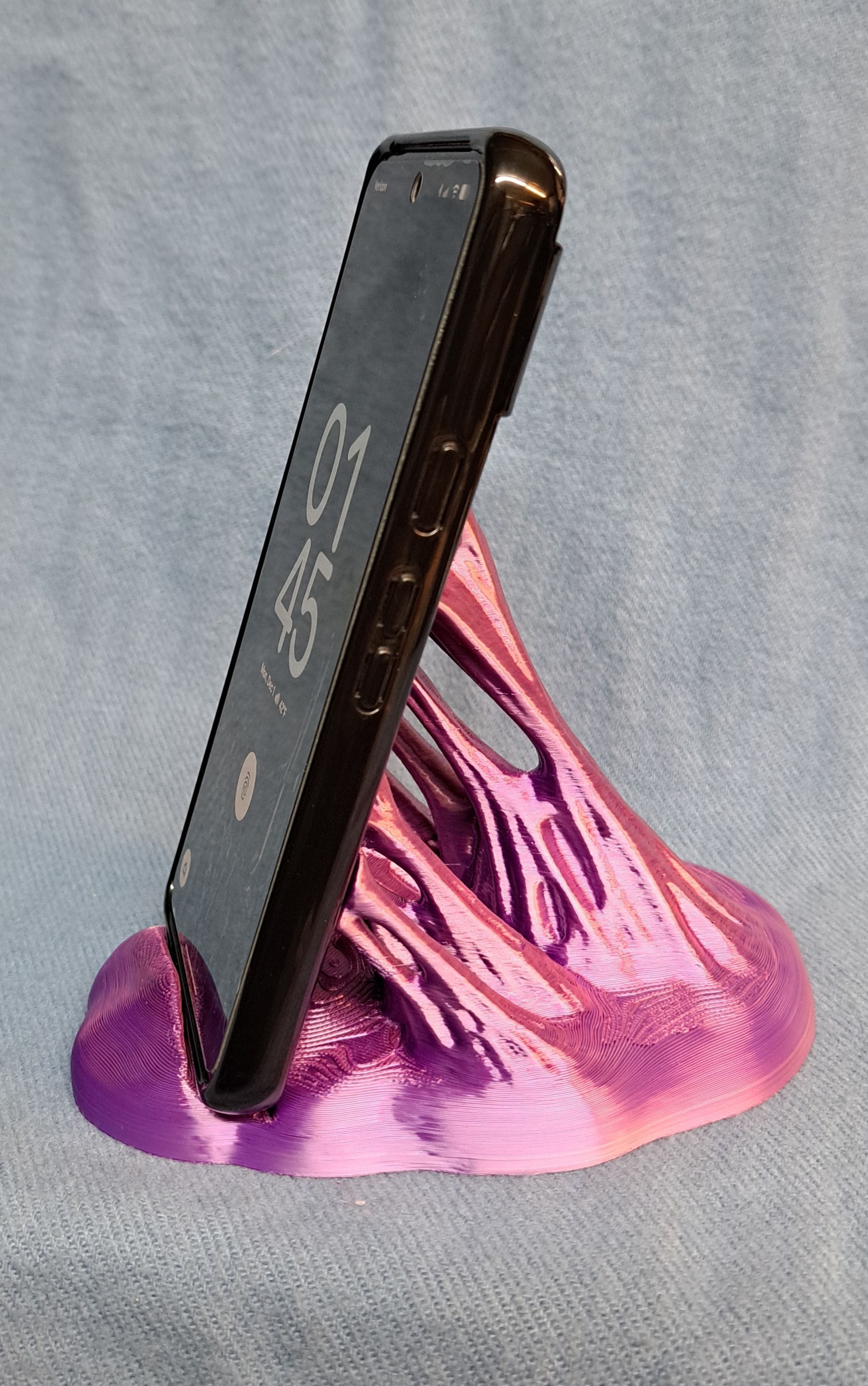 A black smartphone on a pink and purple 3D-printed bubblegum style stand.