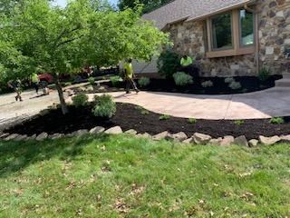 Landscapers installing mulch around a house with a stone exterior and walkway.