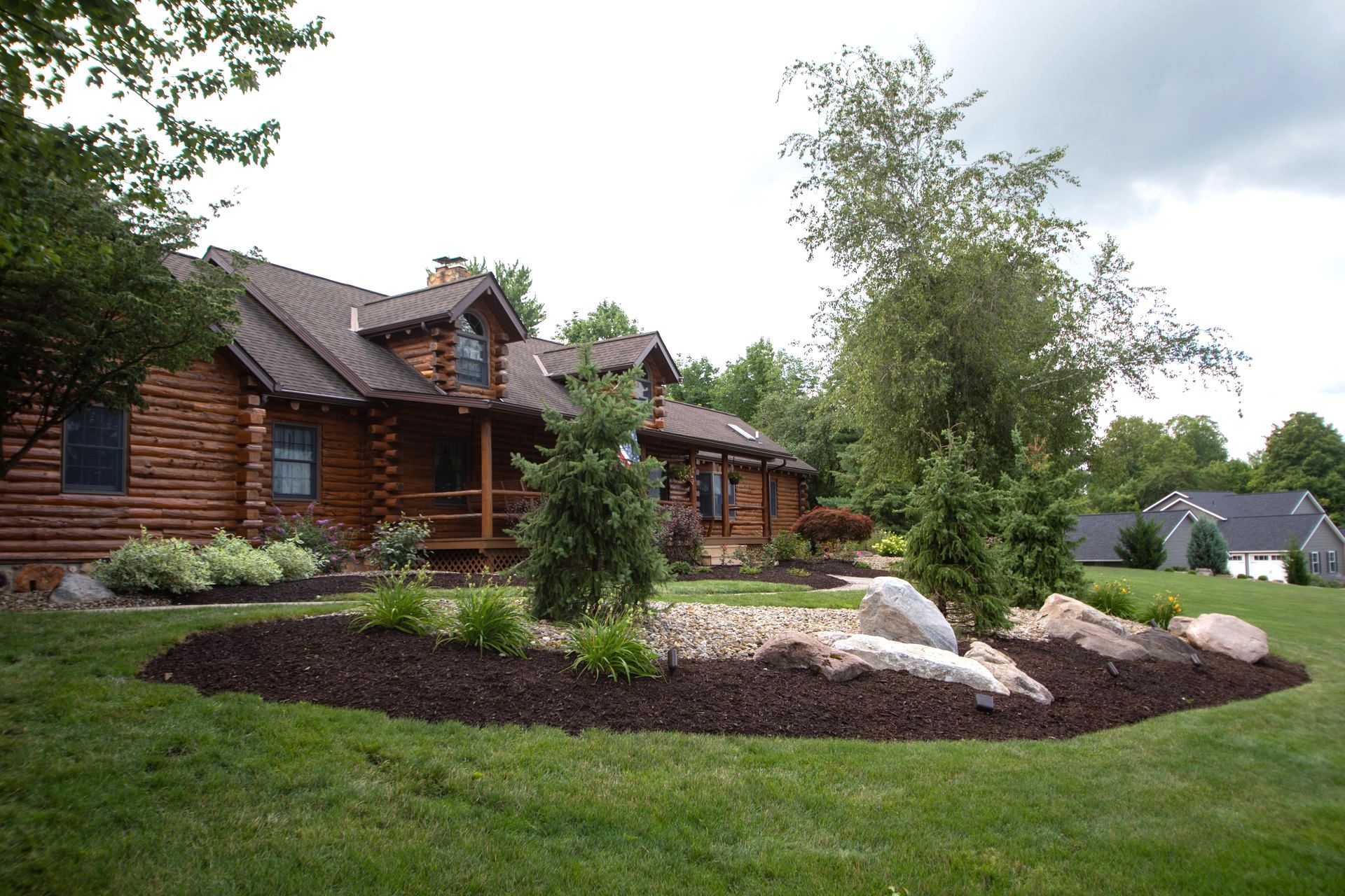 Log cabin home with landscaped front yard, mulch beds, and green grass.