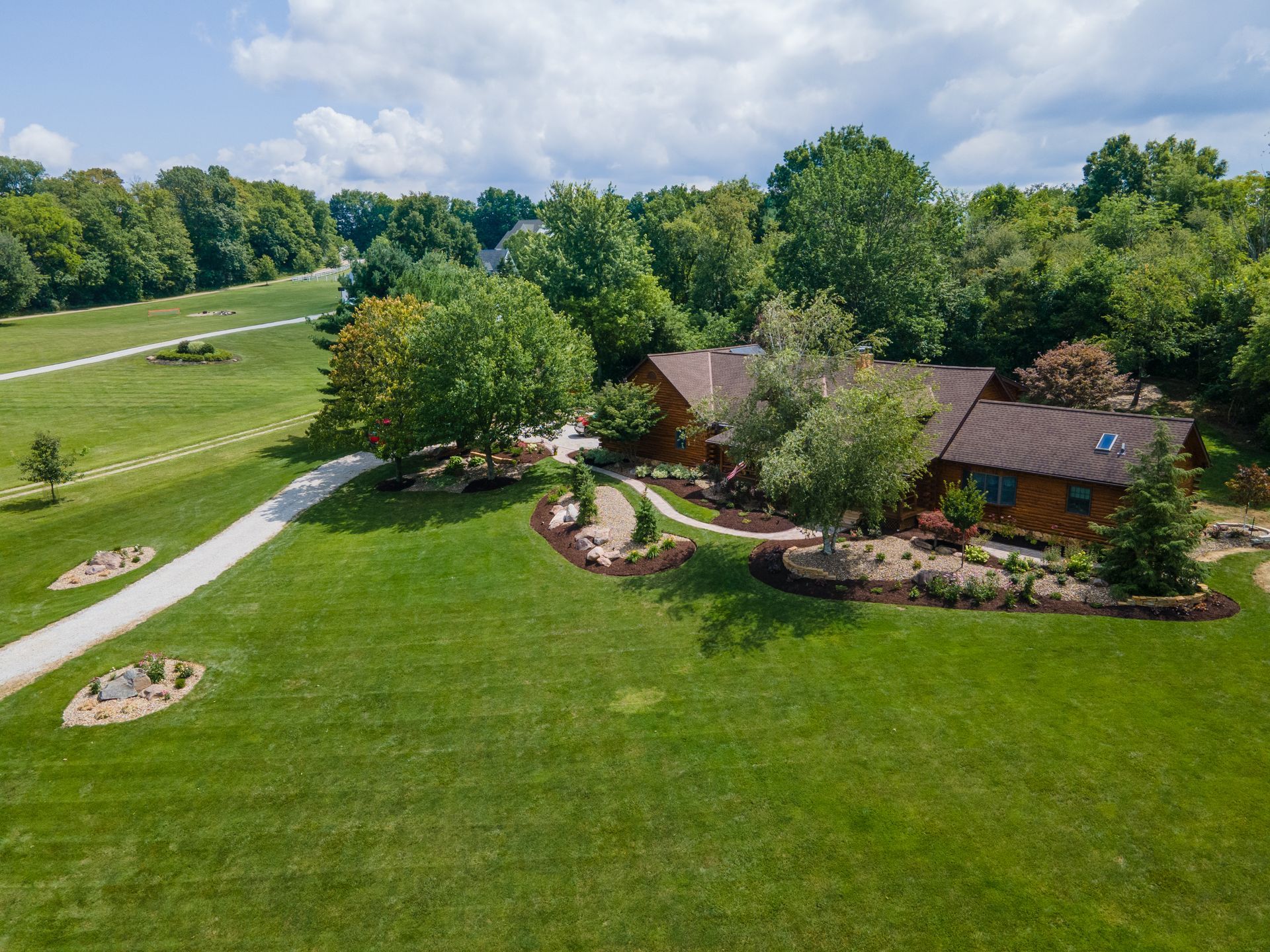 Aerial view of a house with a brown roof and a long driveway, surrounded by green grass and trees.